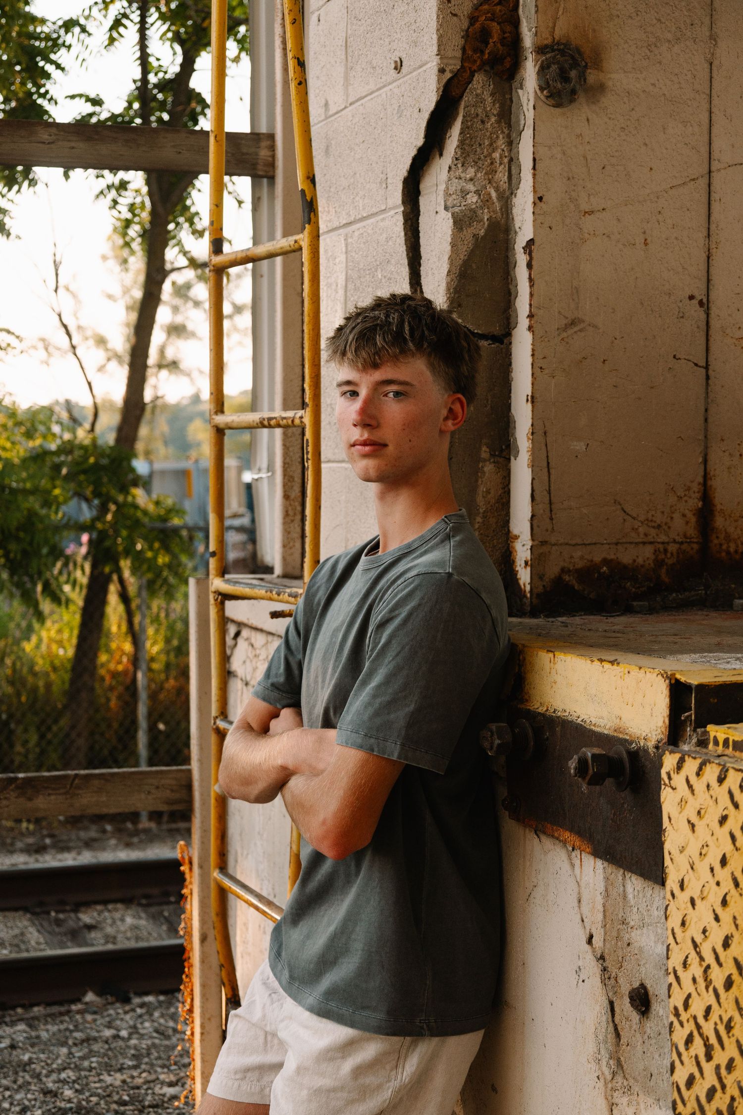 Young man in green t-shirt leans against weathered wall near yellow scaffolding outdoors.