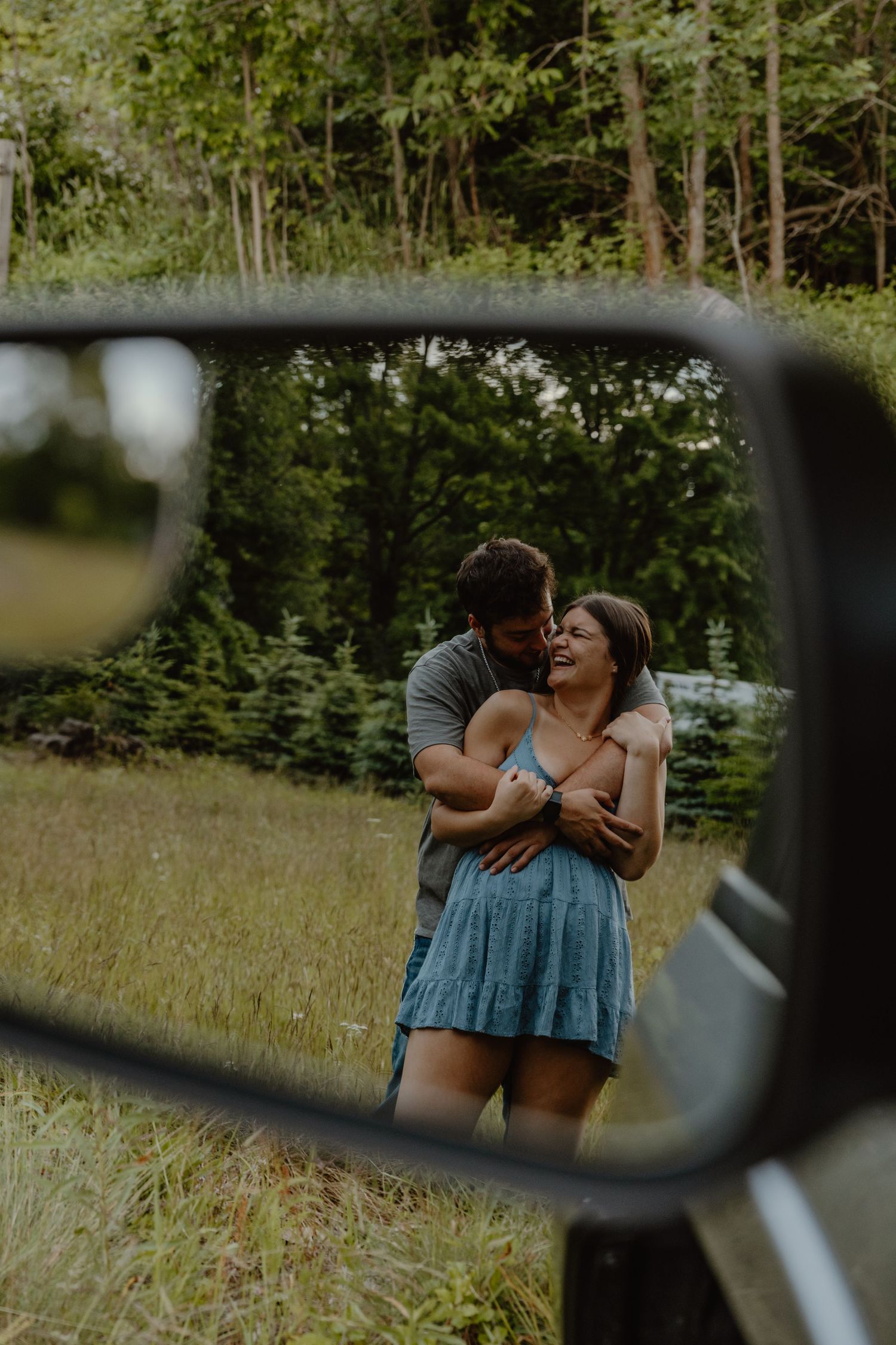 Couple embracing and smiling in a green meadow, captured through a truck side mirror reflection.