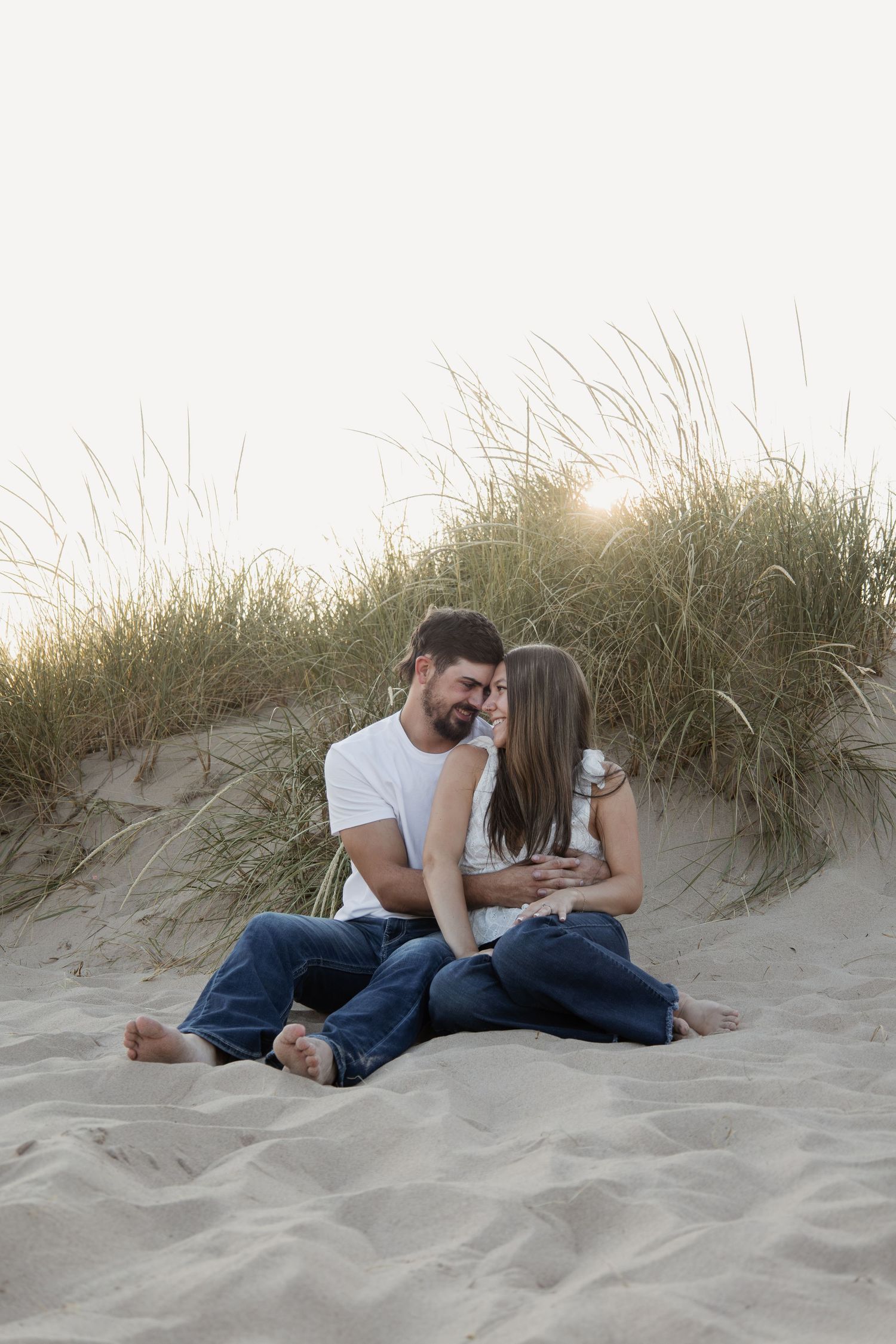 Romantic couple sitting on sand dunes at sunset, gazing at each other affectionately.