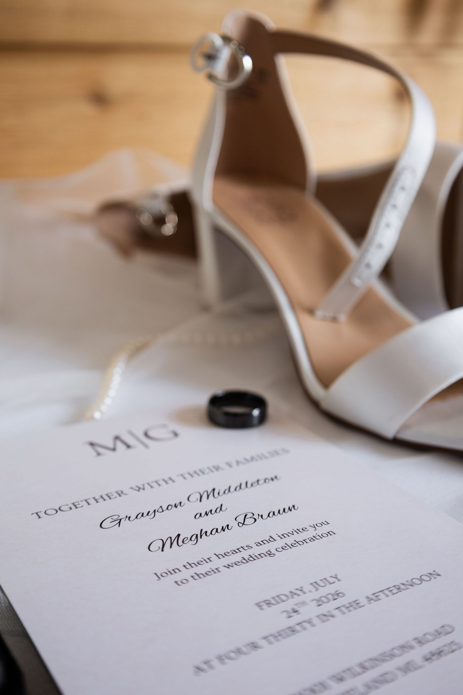Wedding invitation for Grayson Middleton and Meghan Braun with white heels and black ring on marble.