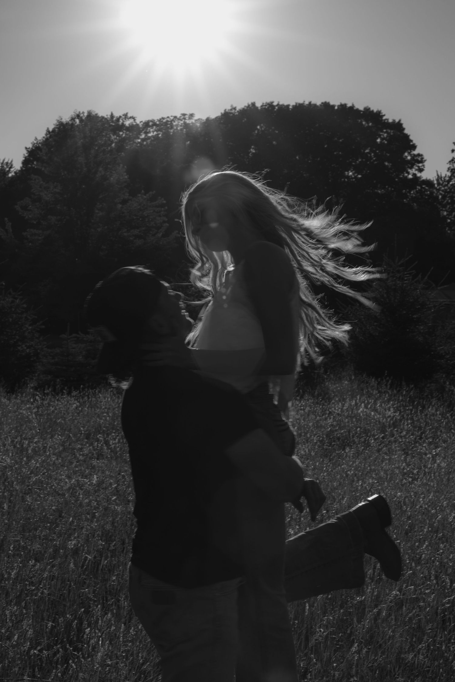 Black and white silhouette of couple embracing in a sunlit field, womans hair flowing in the breeze.
