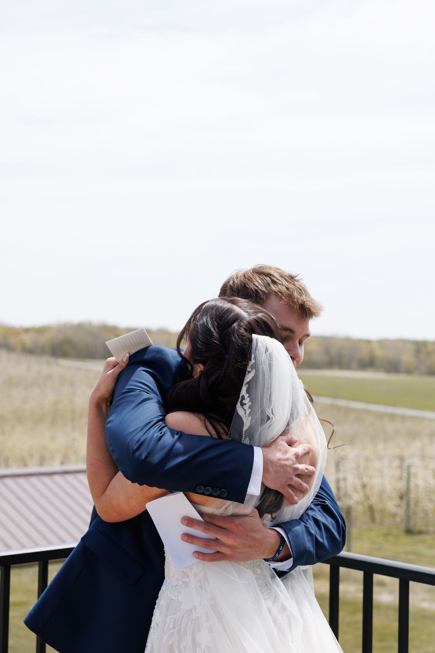 Bride and groom share an emotional hug on an outdoor balcony after exchanging personal vows.