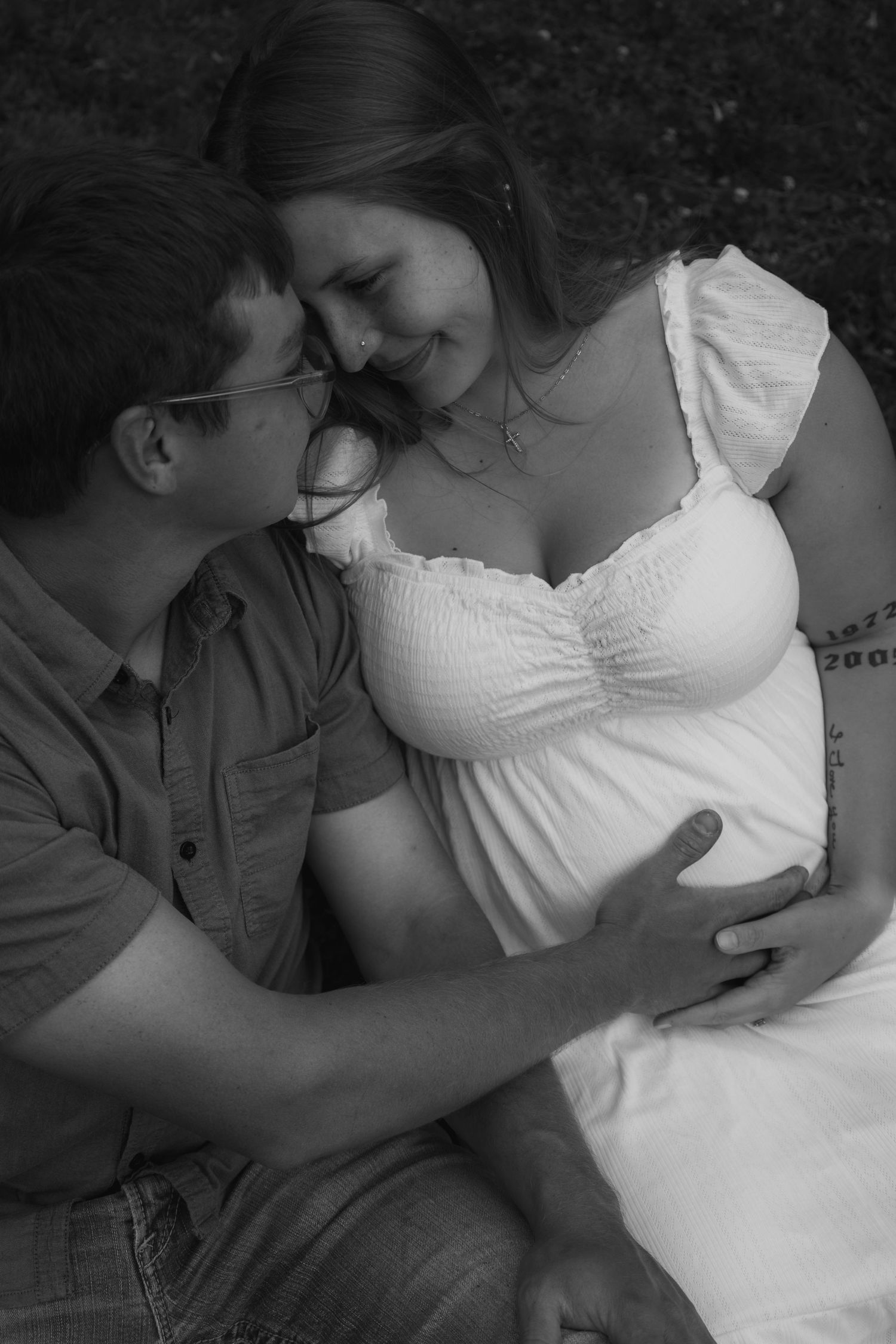 Black and white intimate photo of couple sitting together, man tenderly touching pregnant womans baby bump.