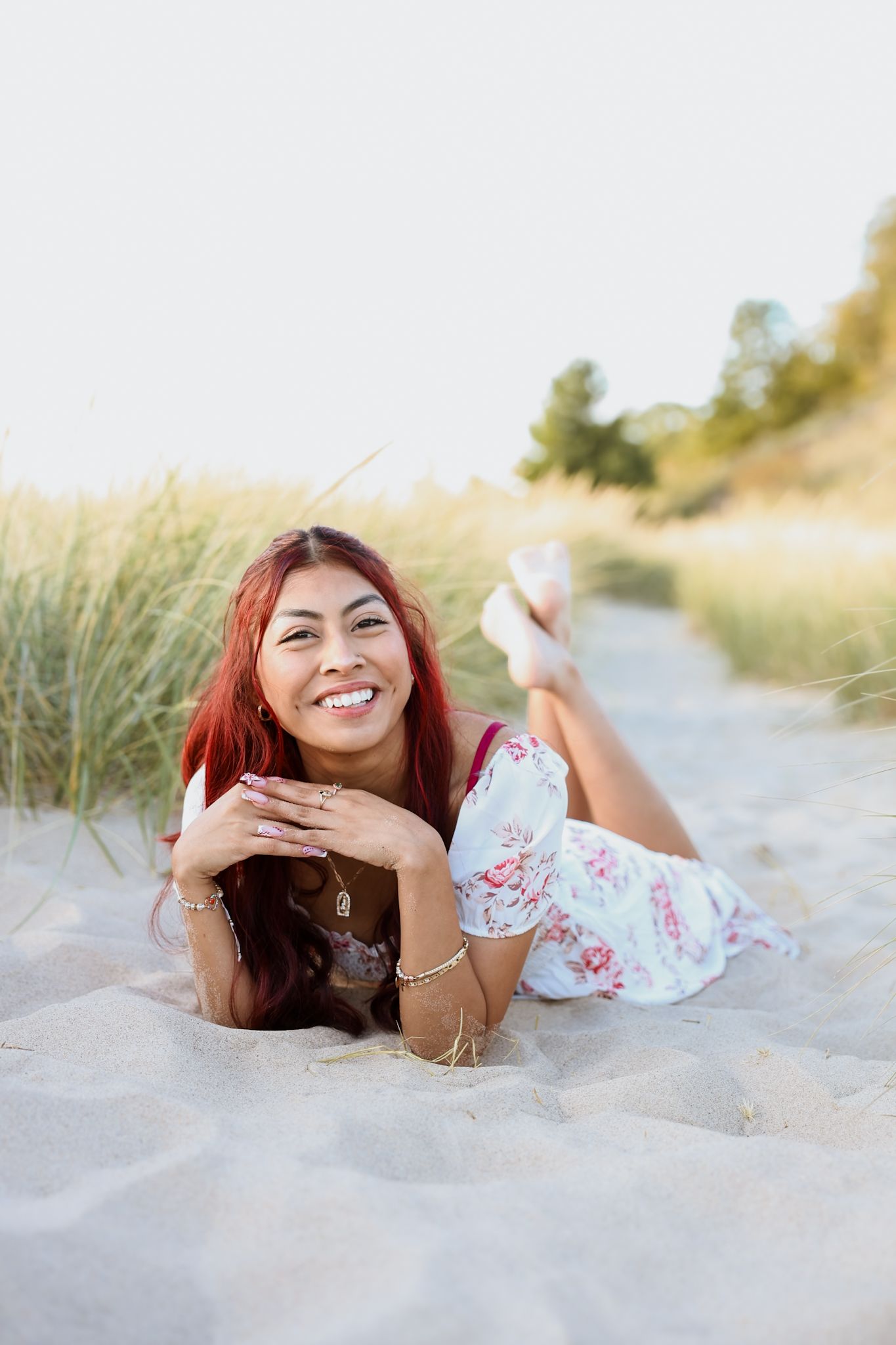 Smiling young woman in floral dress lying on sandy beach dunes.