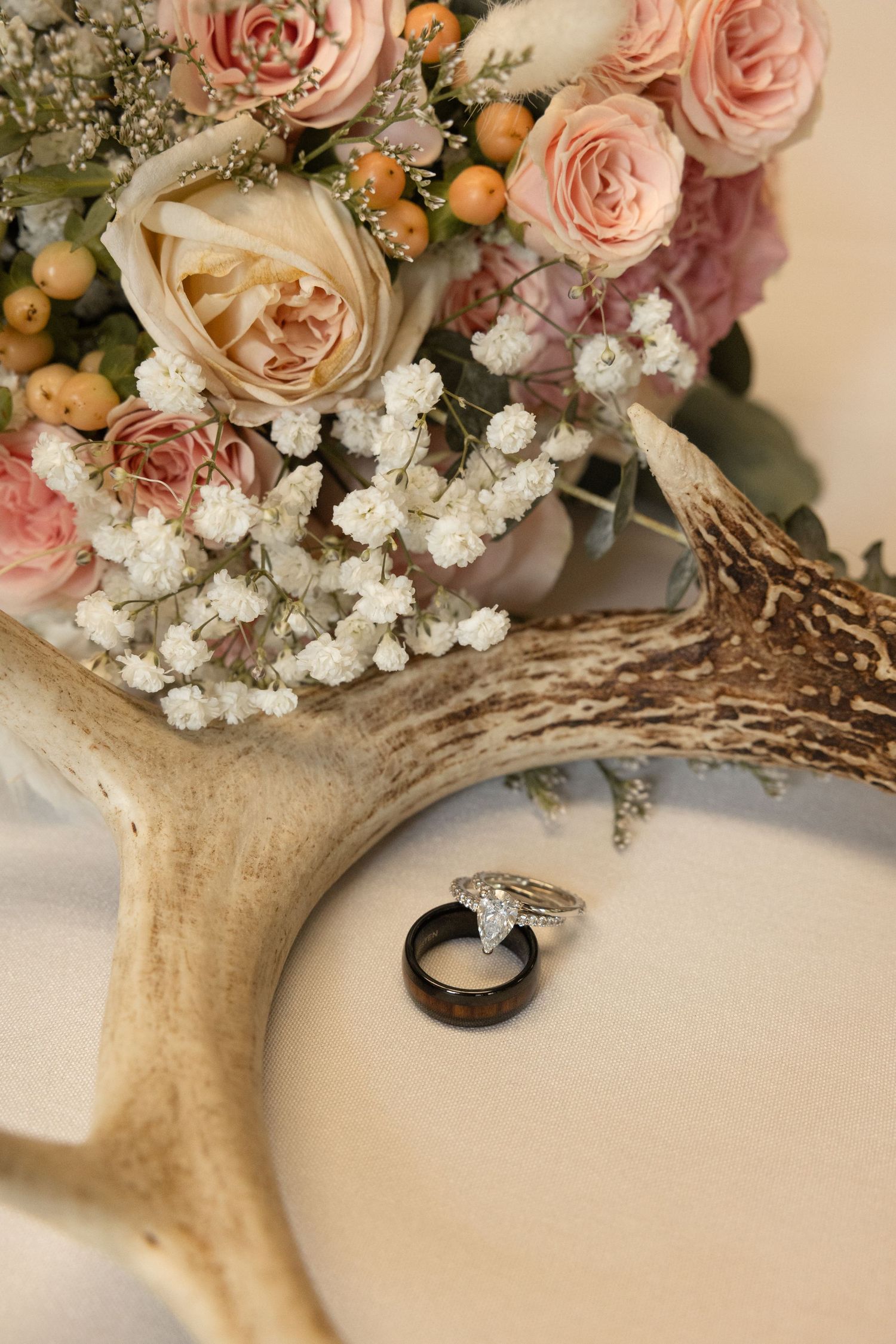 Wedding rings rest on a deer antler beside a bouquet of pink roses and baby's breath.