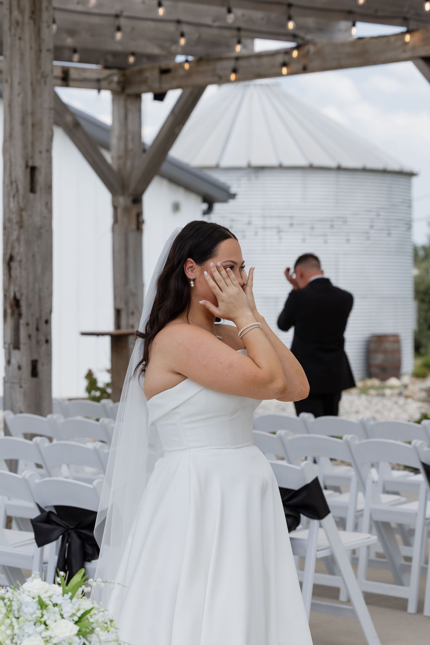 Emotional bride in strapless white gown covers her face with hands during outdoor wedding first look ceremony.