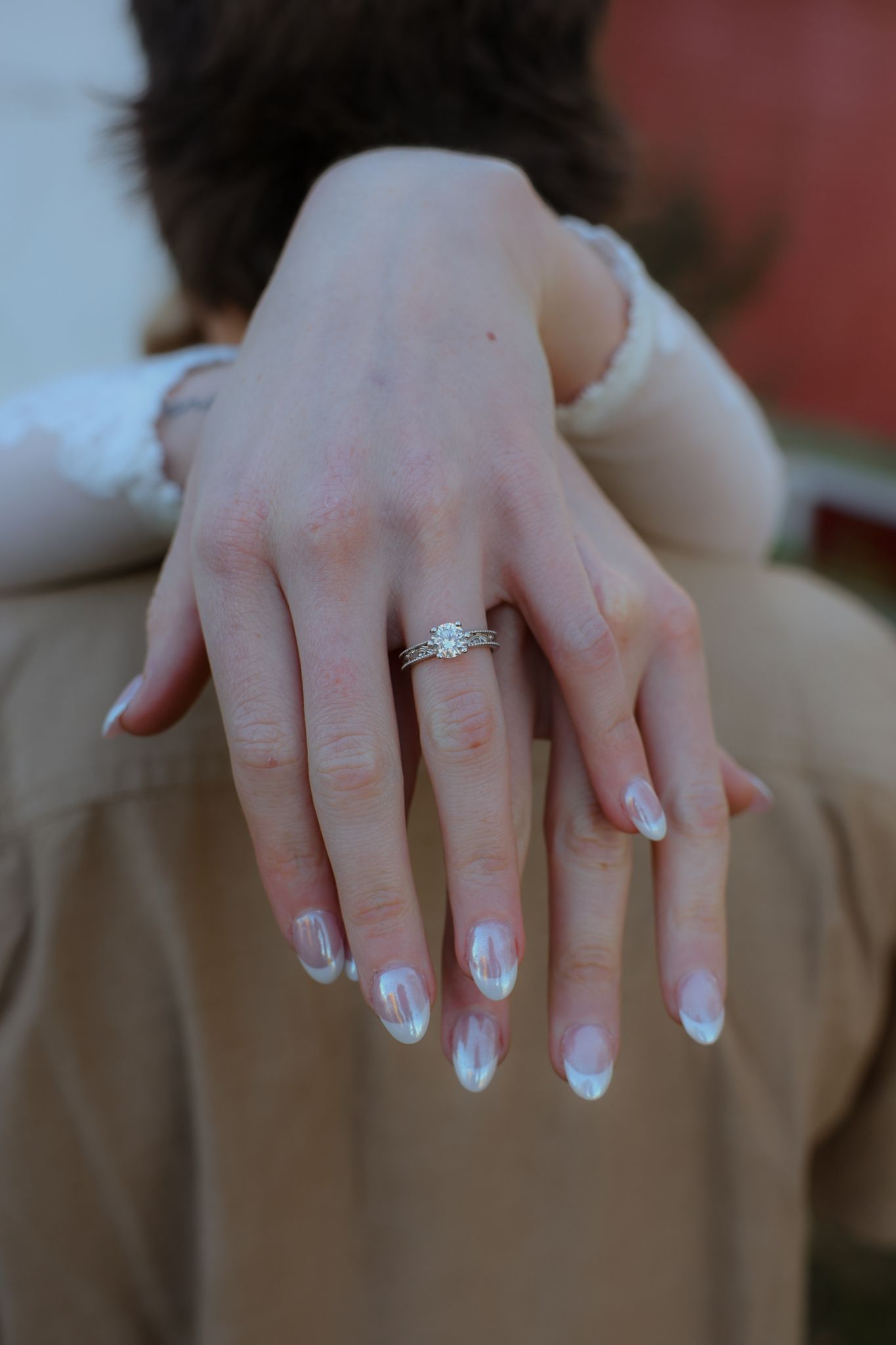 Close-up of a woman's hand displaying a diamond solitaire engagement ring with white French tip nails.