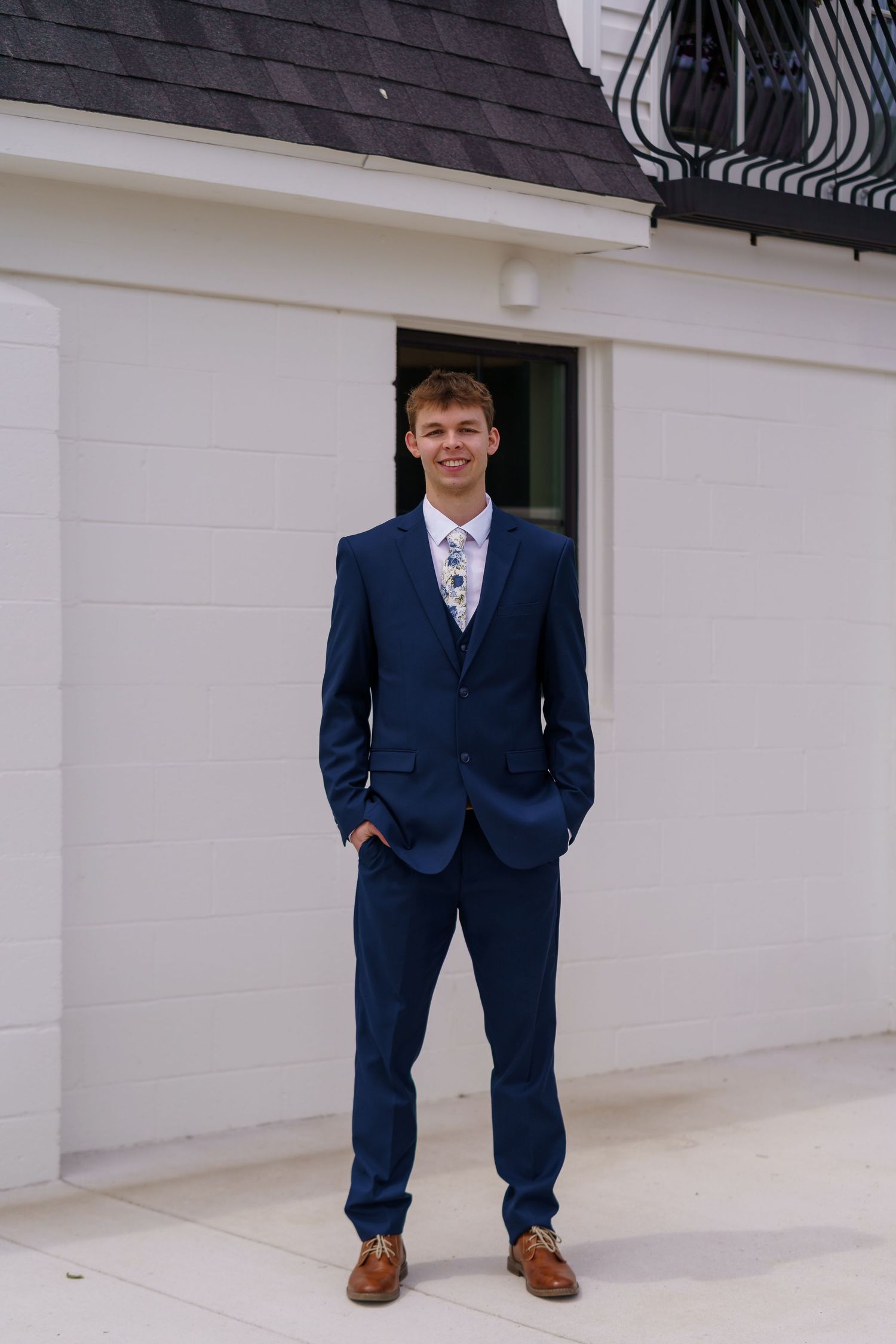 Young groom in navy blue three-piece suit standing confidently in front of a white building.