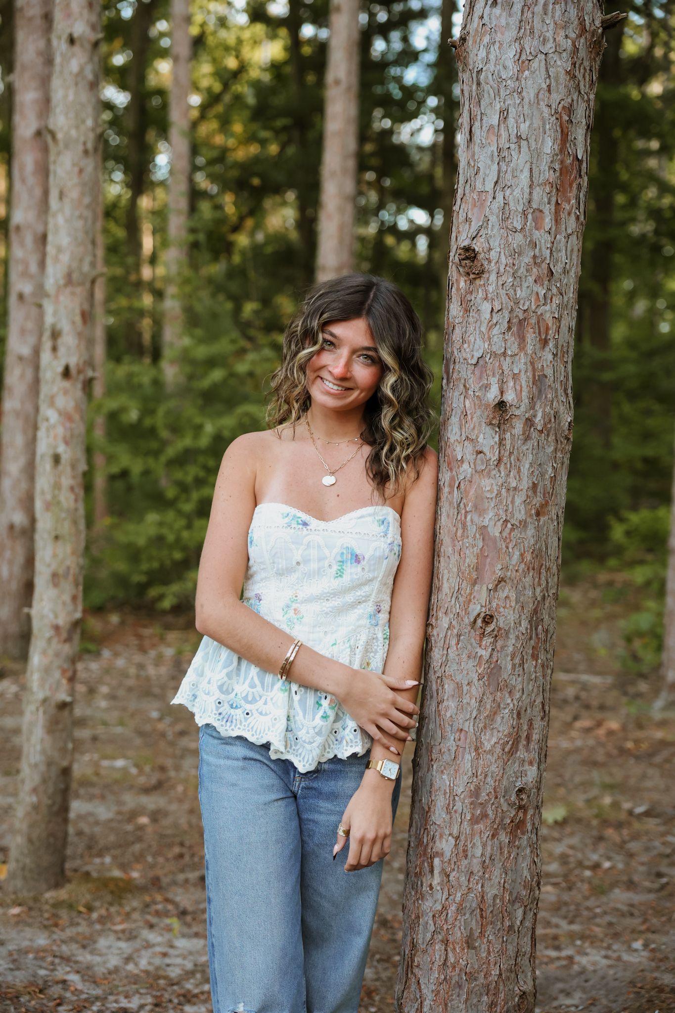Young woman in floral top leaning against pine tree in forest.