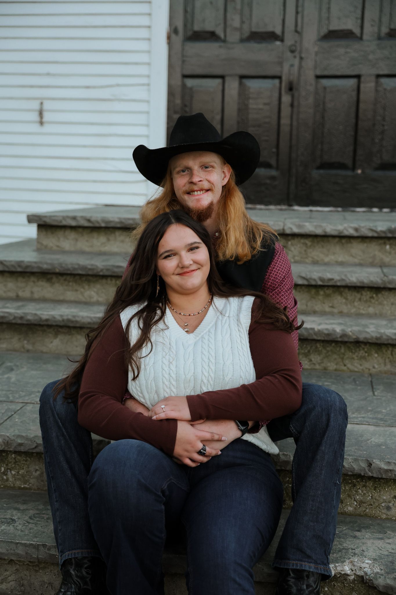 Couple sitting on stone steps, man in black cowboy hat embracing woman from behind.