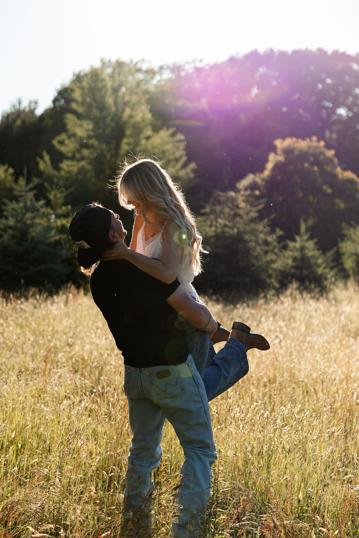 A couple shares a romantic moment in a sunlit golden field, man lifting woman.