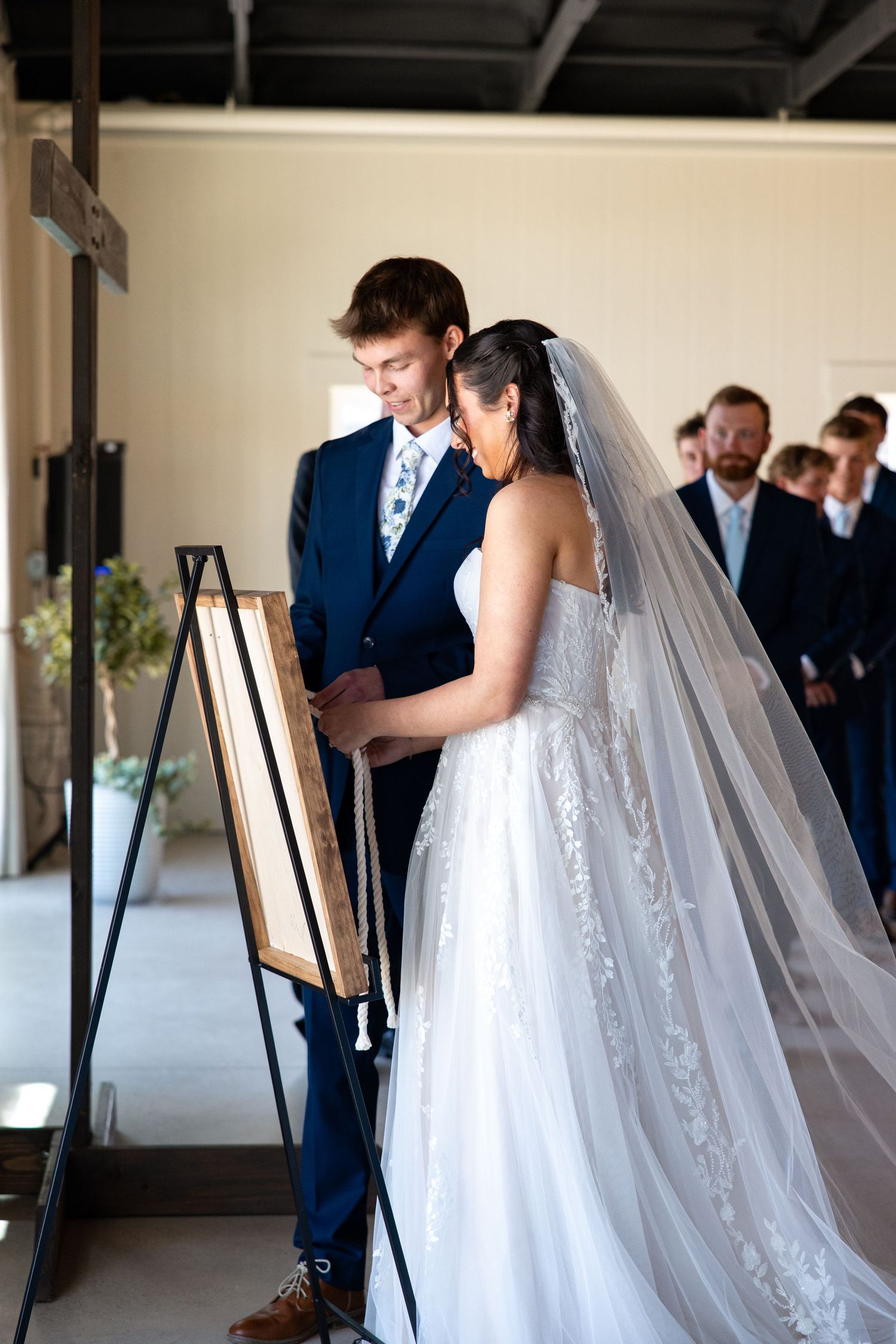 Bride and groom participate in cord of three strands unity ceremony at indoor wedding.