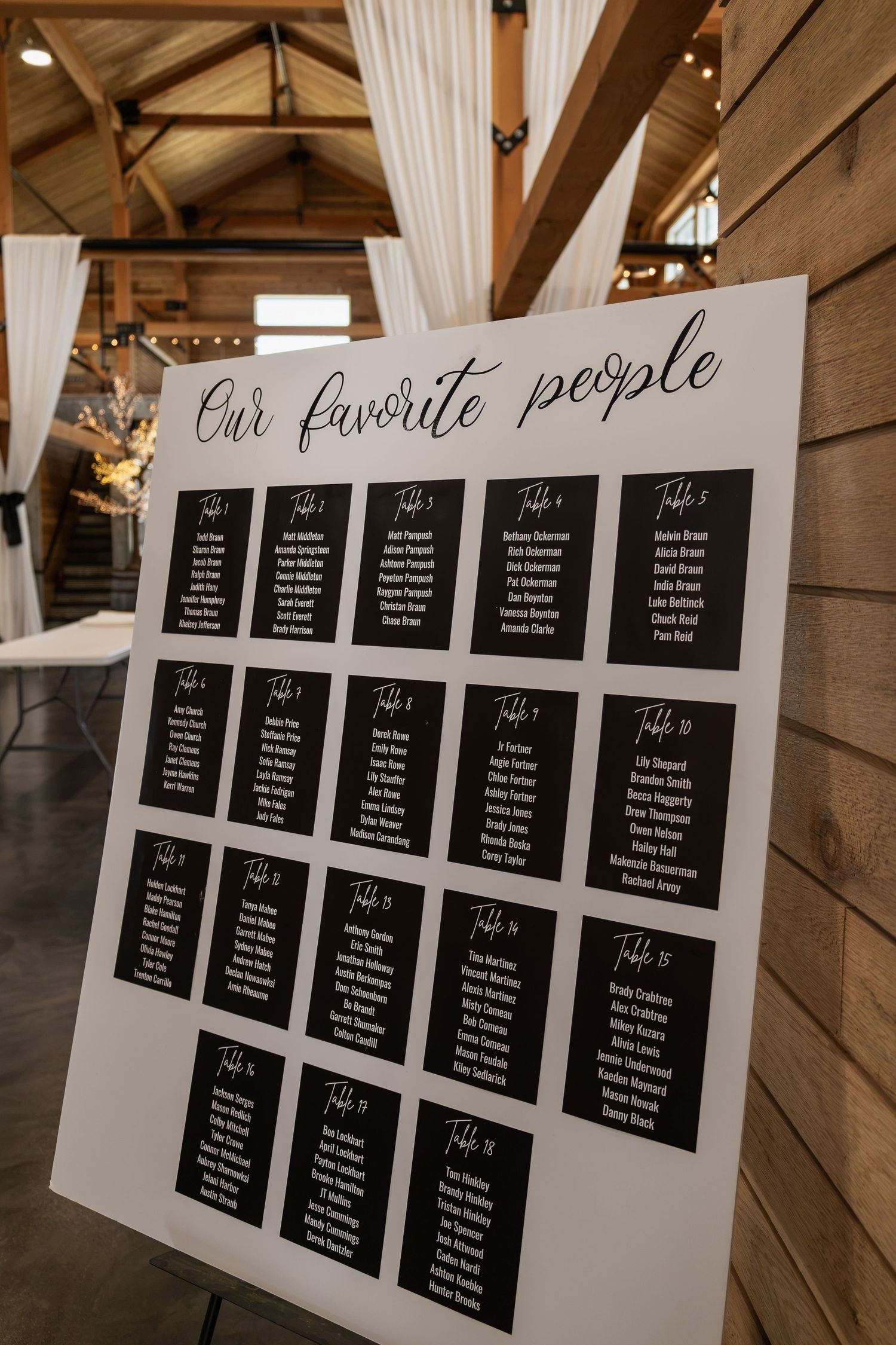 Elegant wedding seating chart board titled Our Favorite People displayed on easel in rustic barn venue.