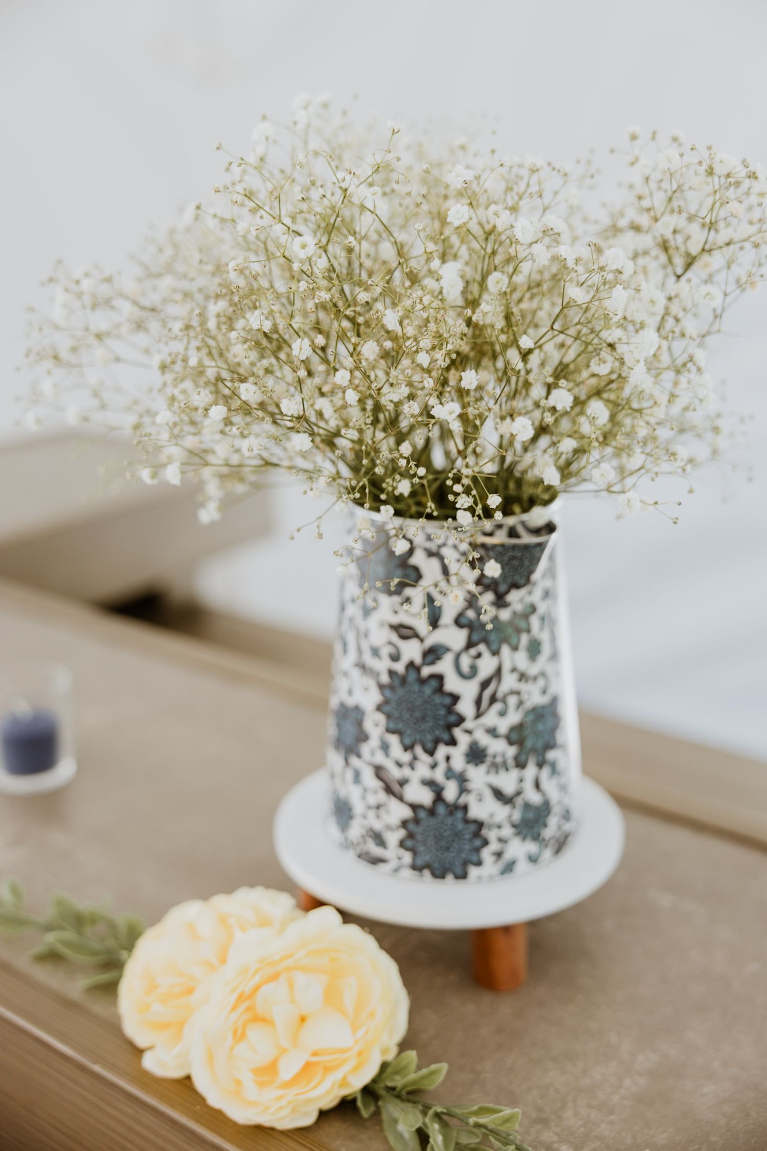 Delicate baby's breath arrangement in floral patterned vase with yellow roses at wedding reception.