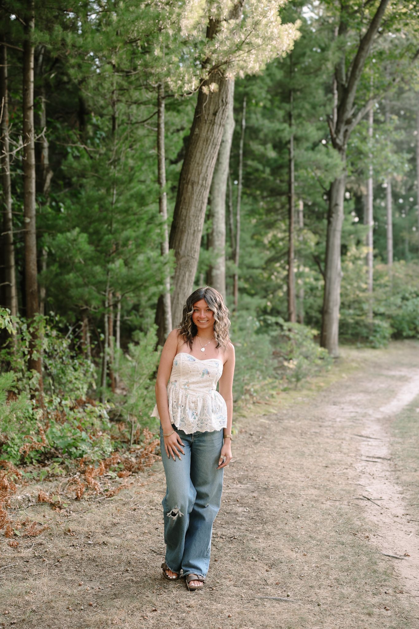Young woman in lace top and jeans walking on forest dirt path.