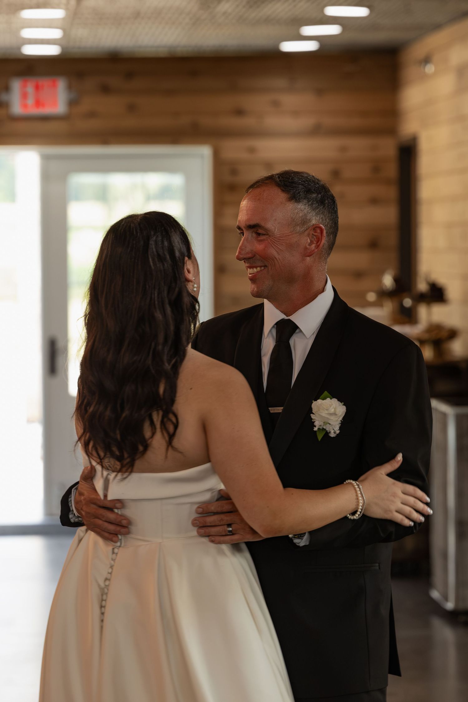Bride and older gentleman sharing a first dance in a warmly lit rustic venue.