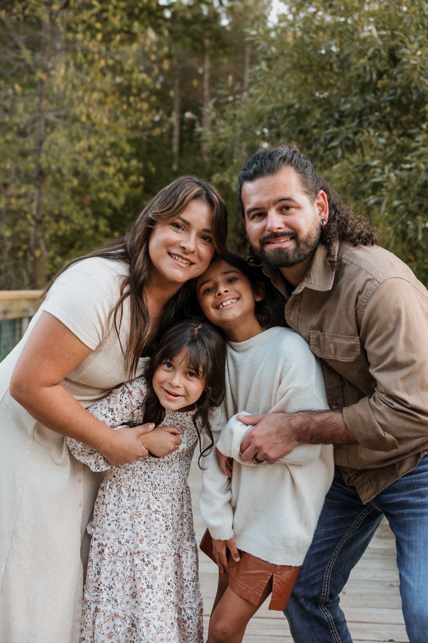 Happy family of four embraces and smiles together on a wooden bridge in the forest.