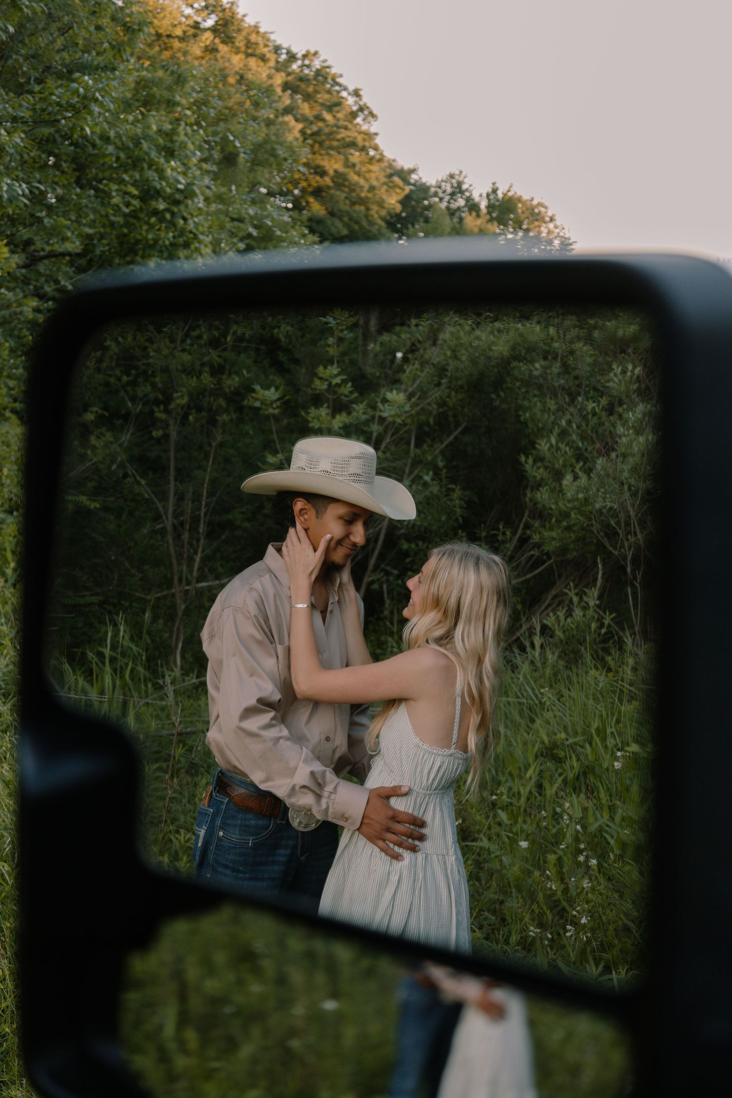 Couple sharing a tender moment reflected in a truck side mirror outdoors.