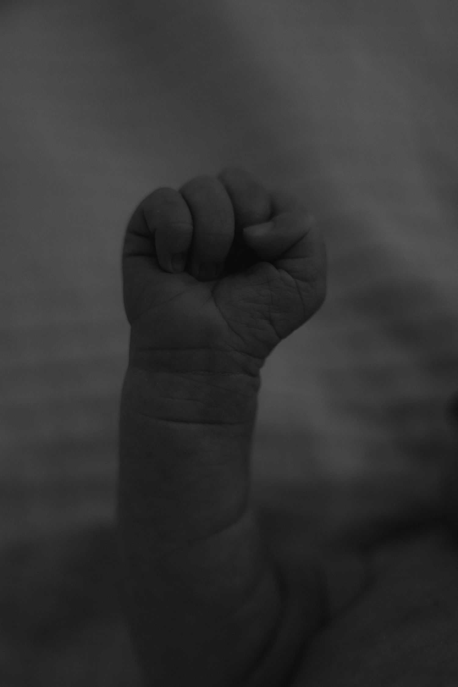 Black and white close-up photo of a newborn baby's tiny clenched fist, showcasing delicate skin and fingers.