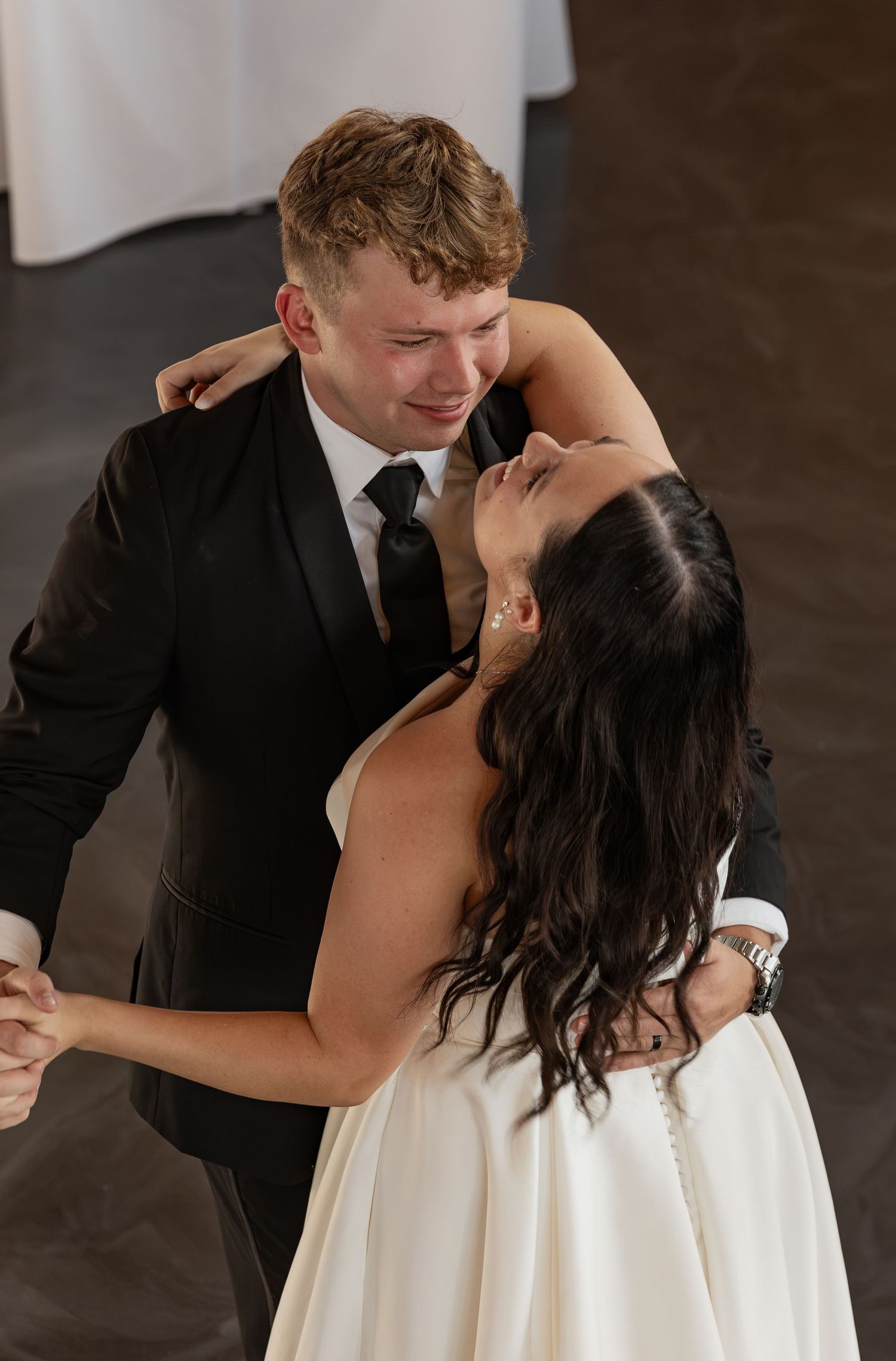 Bride and groom share emotional first dance, gazing at each other lovingly in elegant wedding attire.