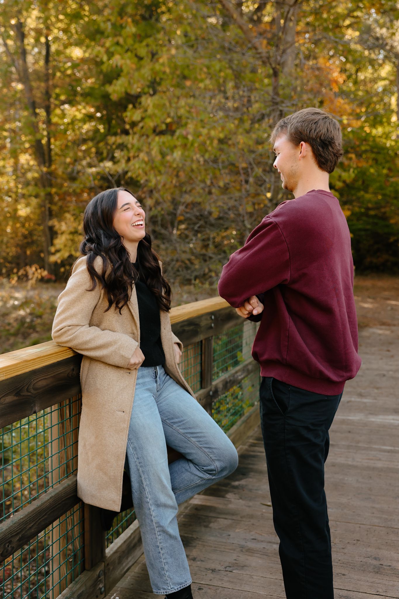 Laughing couple on wooden bridge surrounded by vibrant autumn foliage.