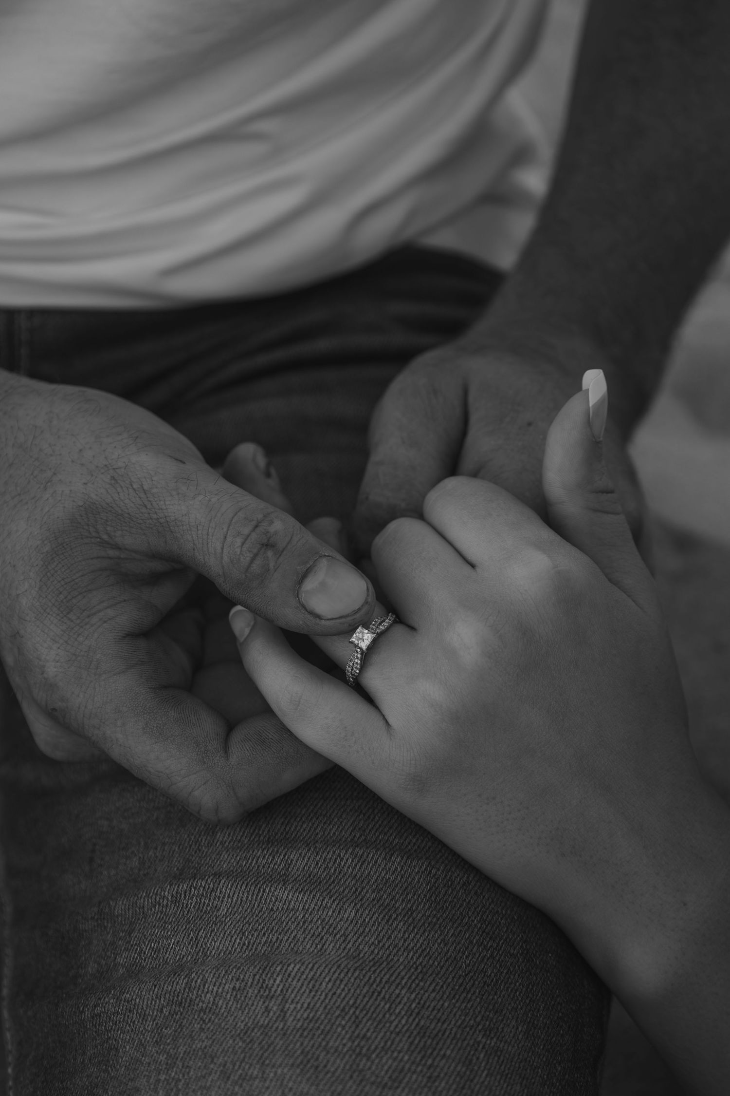 Black and white photo of a couple holding hands with an engagement ring on the woman's finger.