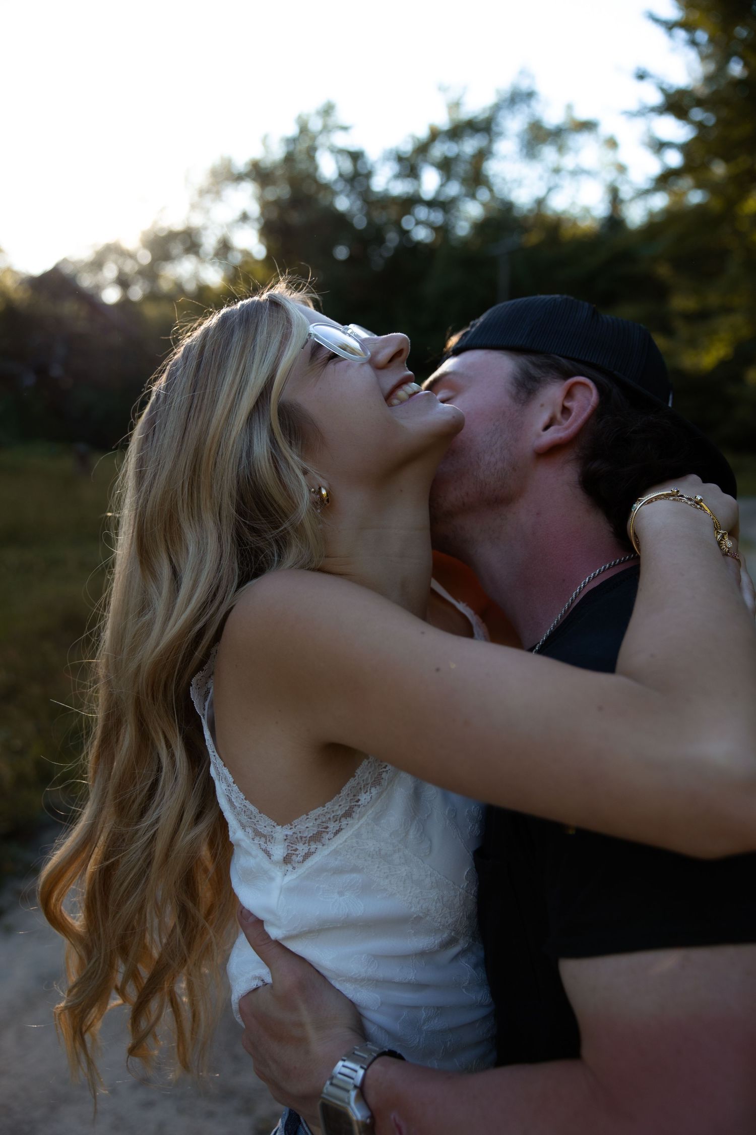 Couple sharing a passionate kiss outdoors at dusk, woman in white lace top with long blonde hair.