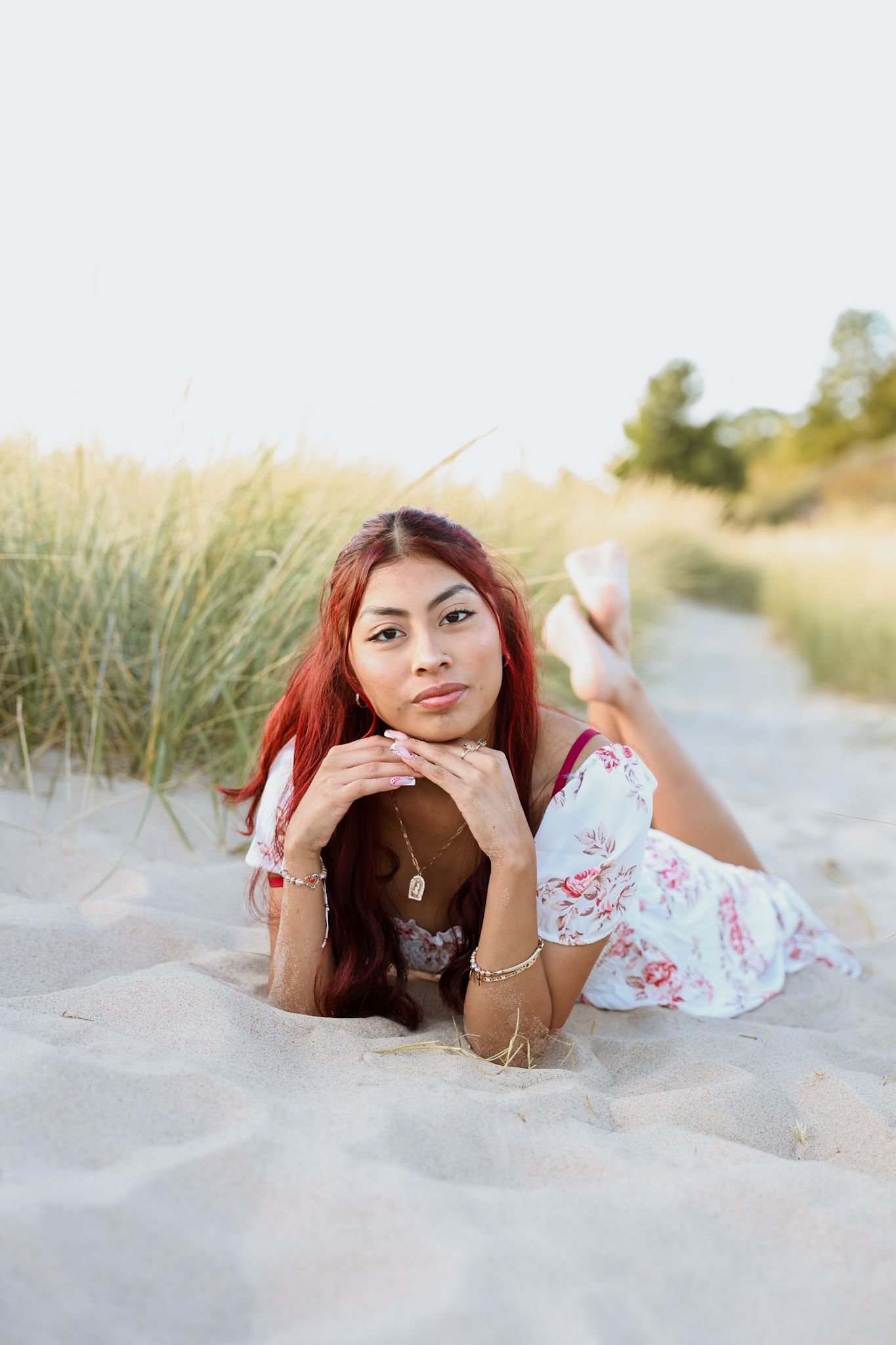 Young woman in floral dress lying on sand between beach grass.