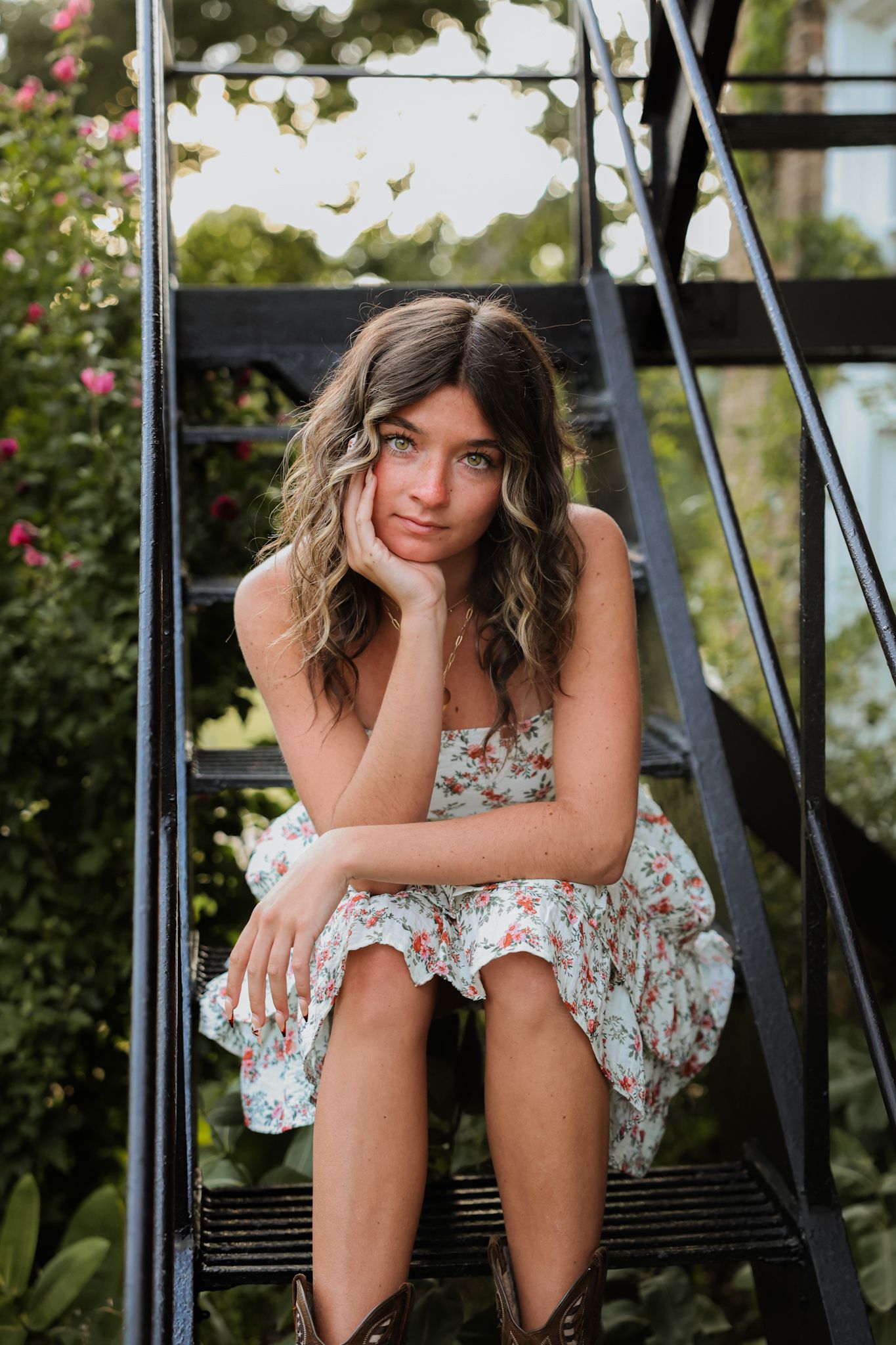 Young woman in floral dress sitting pensively on black metal stairs.
