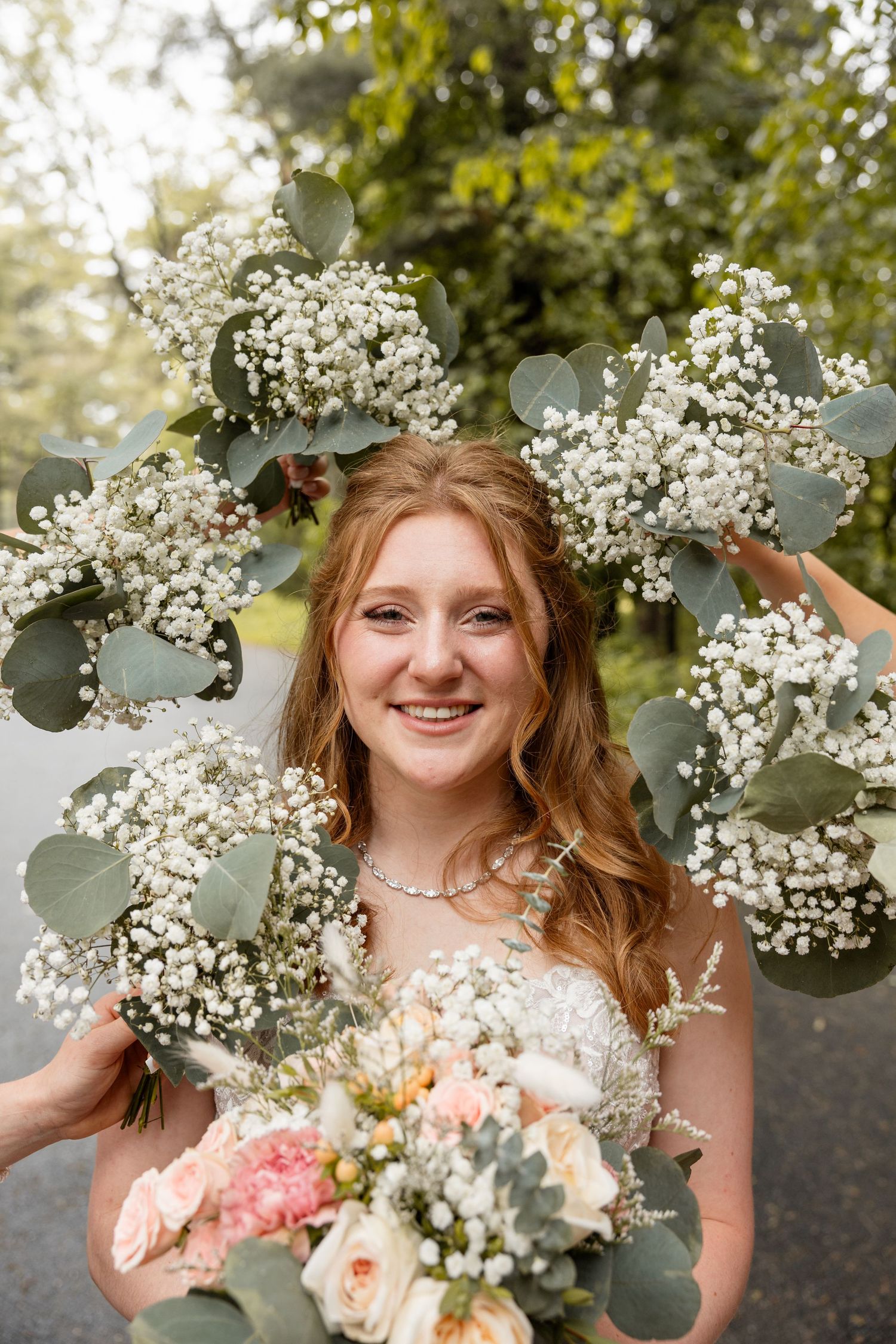 Smiling bride with red hair surrounded by baby's breath and eucalyptus bouquets outdoors.
