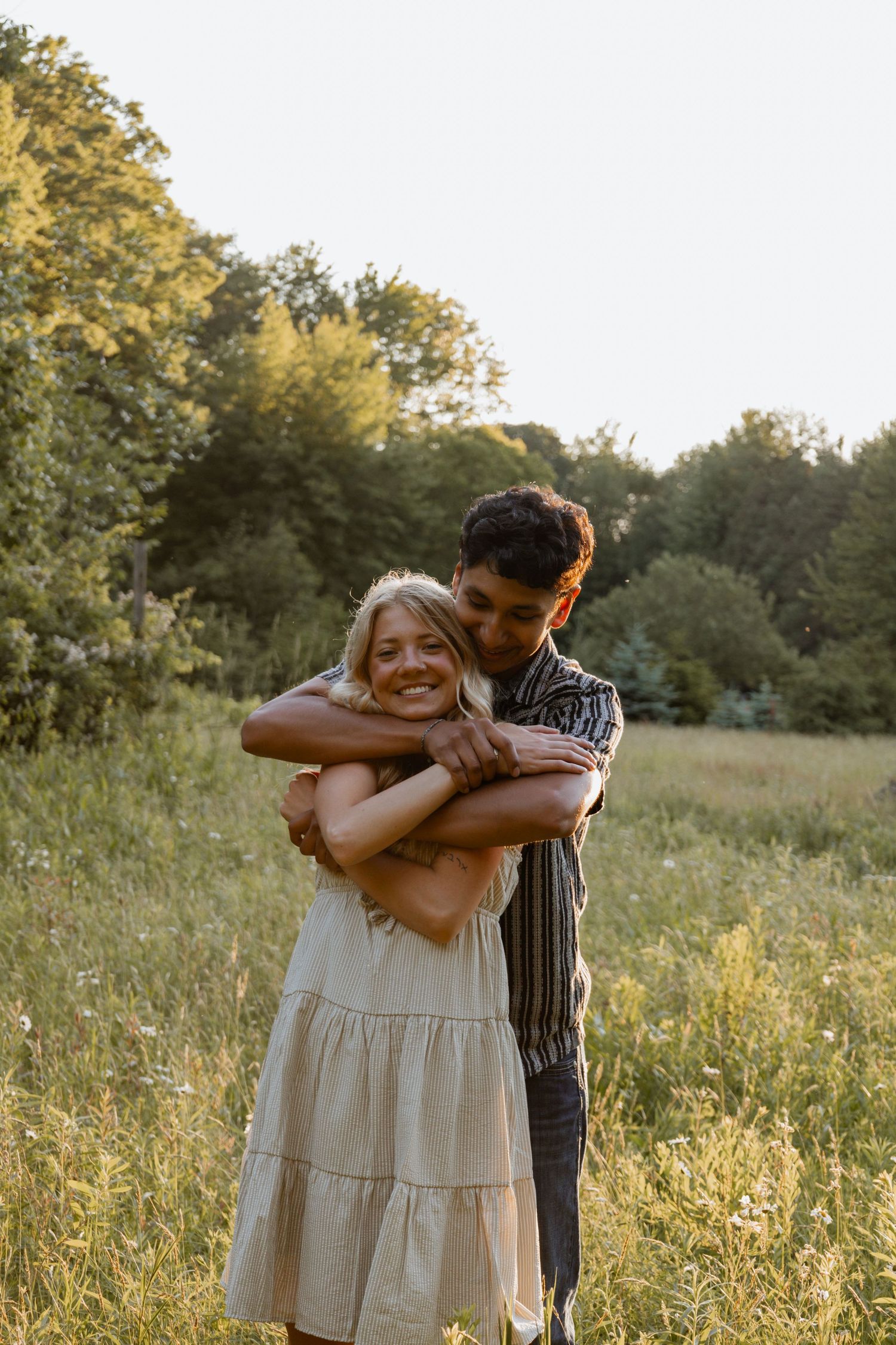 Man embracing smiling woman from behind in a sunny wildflower meadow.
