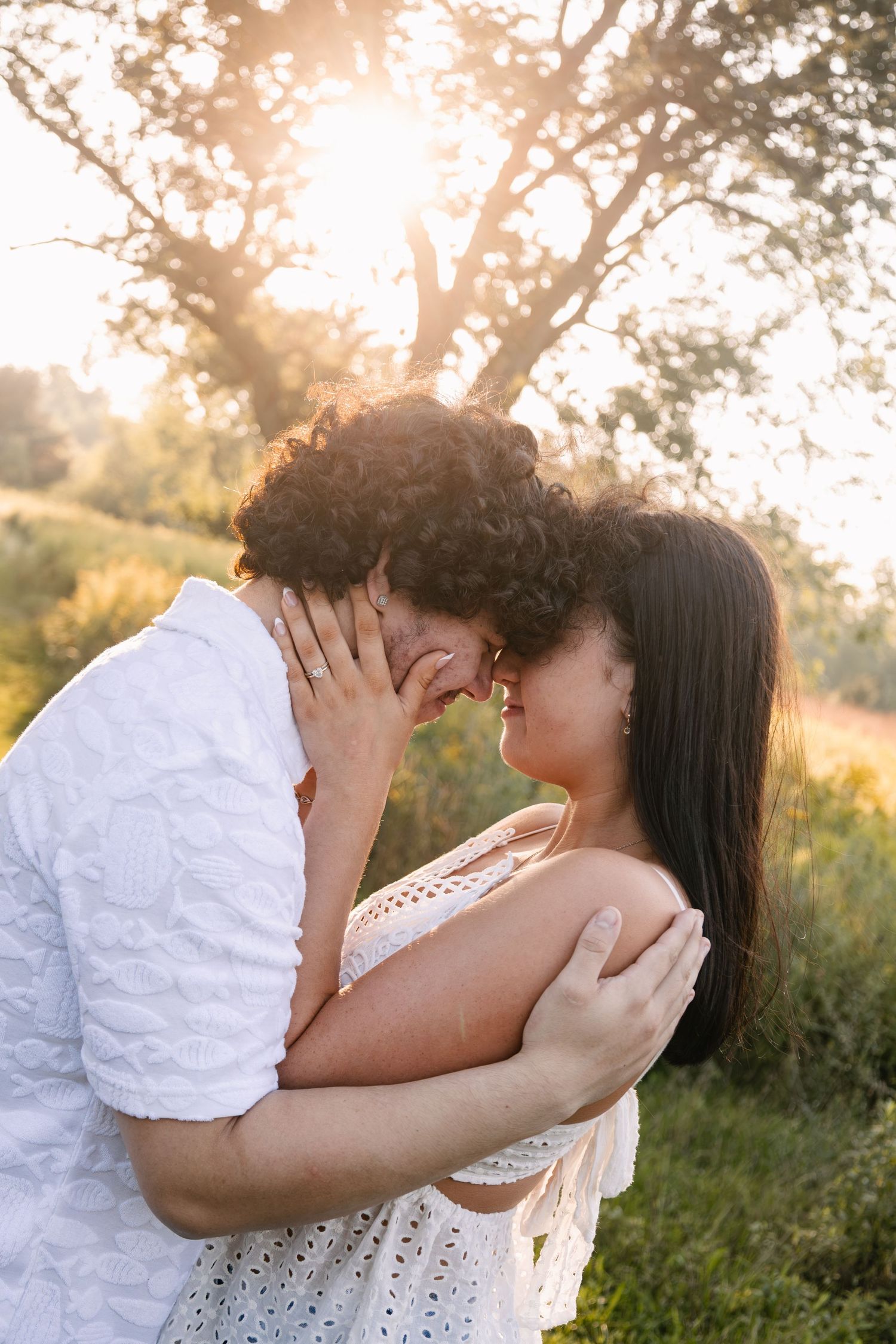 Romantic couple sharing a tender moment outdoors at golden sunset, embracing and about to kiss in a lush green field.