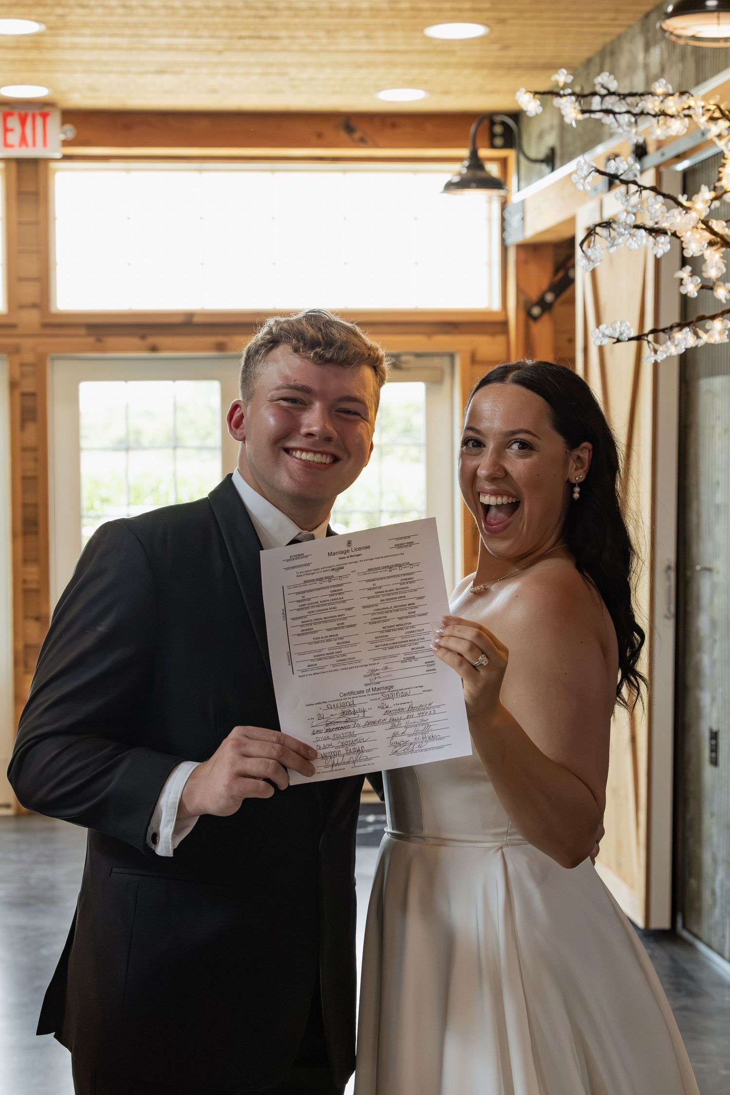 Joyful newlyweds holding their marriage certificate in a rustic wedding venue.