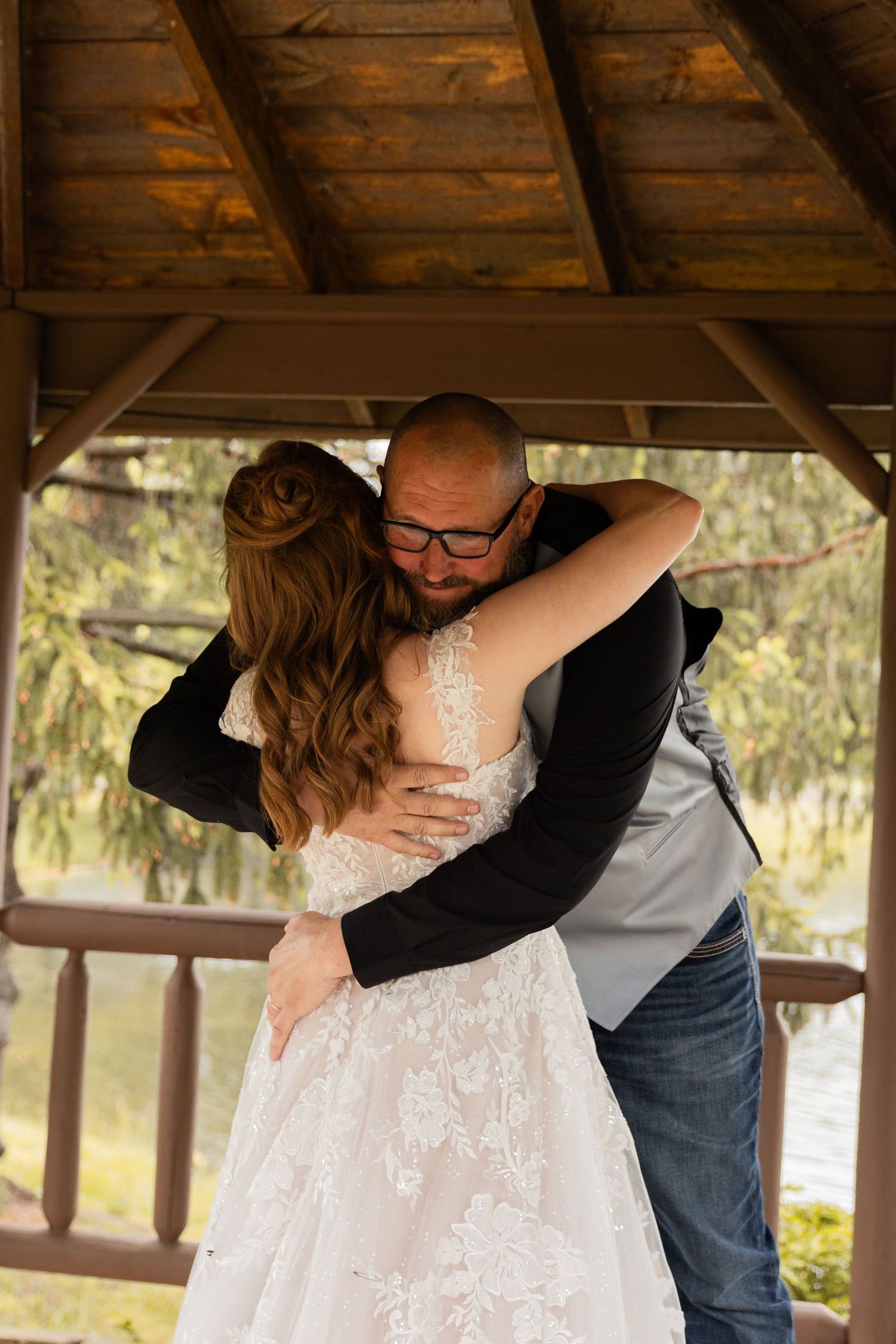 Bride and groom share a tender embrace under a wooden gazebo during their wedding day.