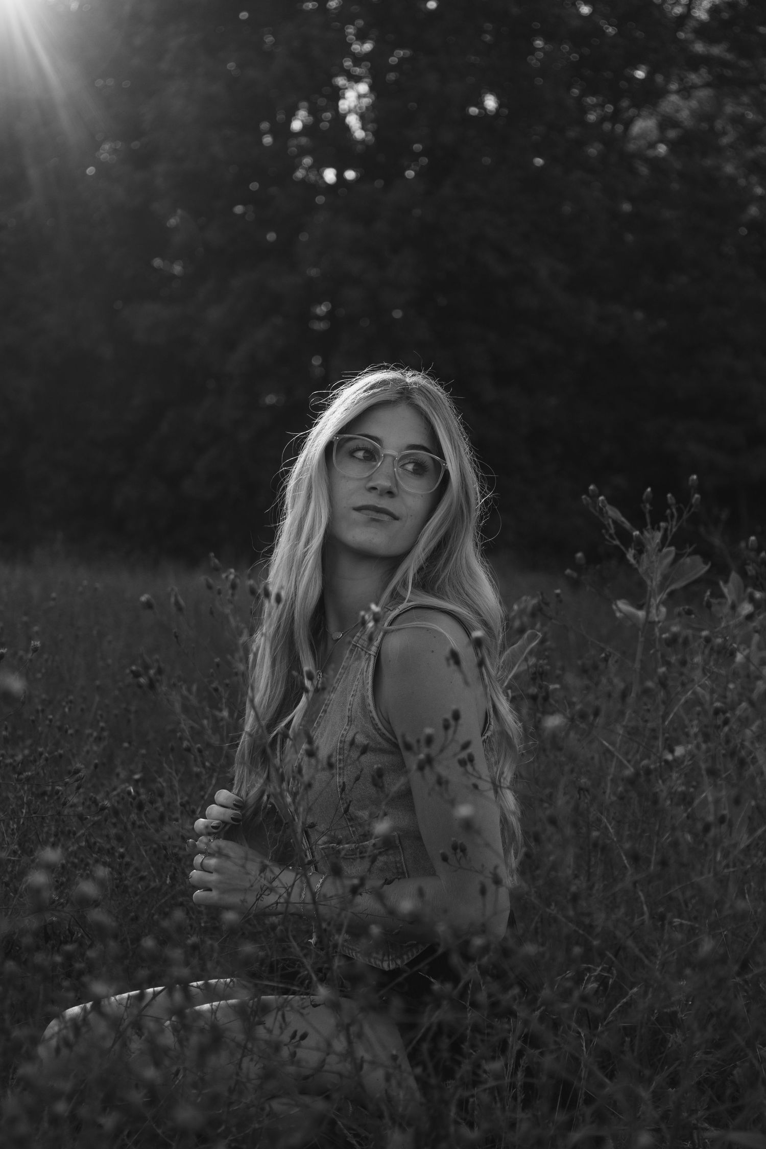 Blonde woman with glasses sitting in a field of wildflowers in a dreamy black and white photo.