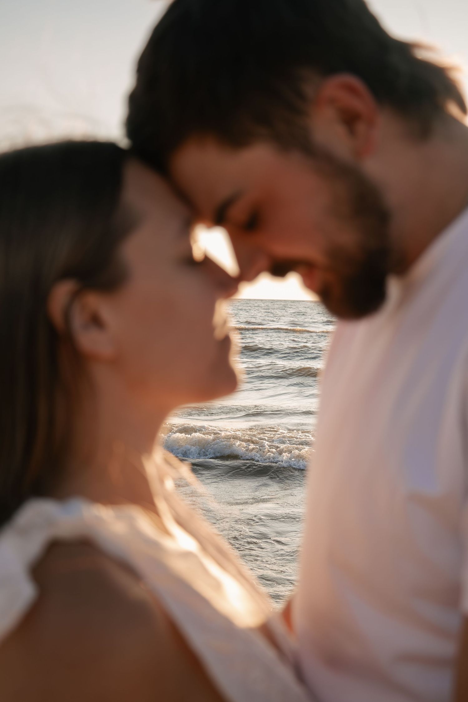 Romantic couple sharing an intimate moment at sunset beach, faces close together with ocean waves in the background.