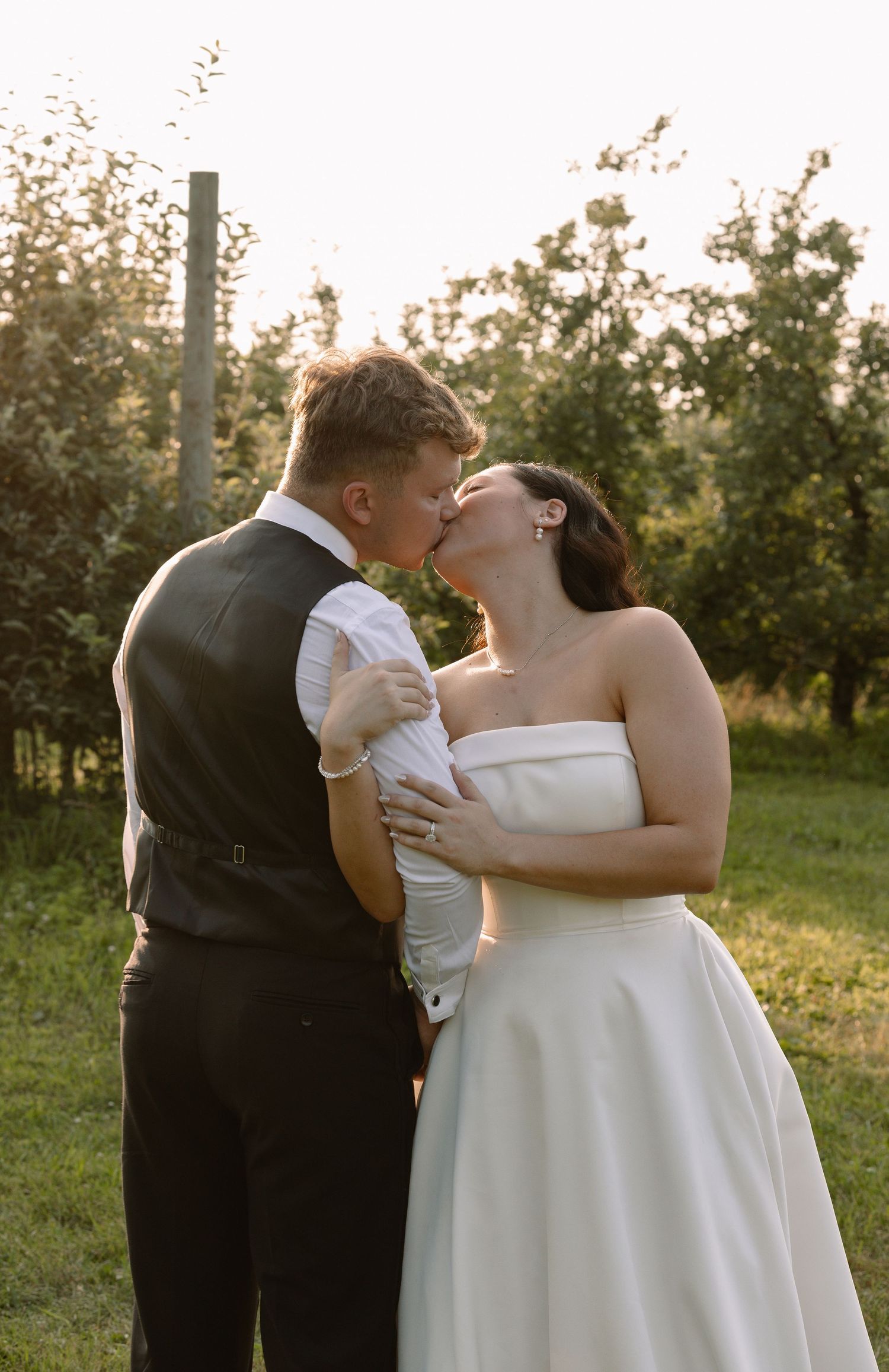 Bride and groom share a romantic golden hour kiss in an orchard on their wedding day.