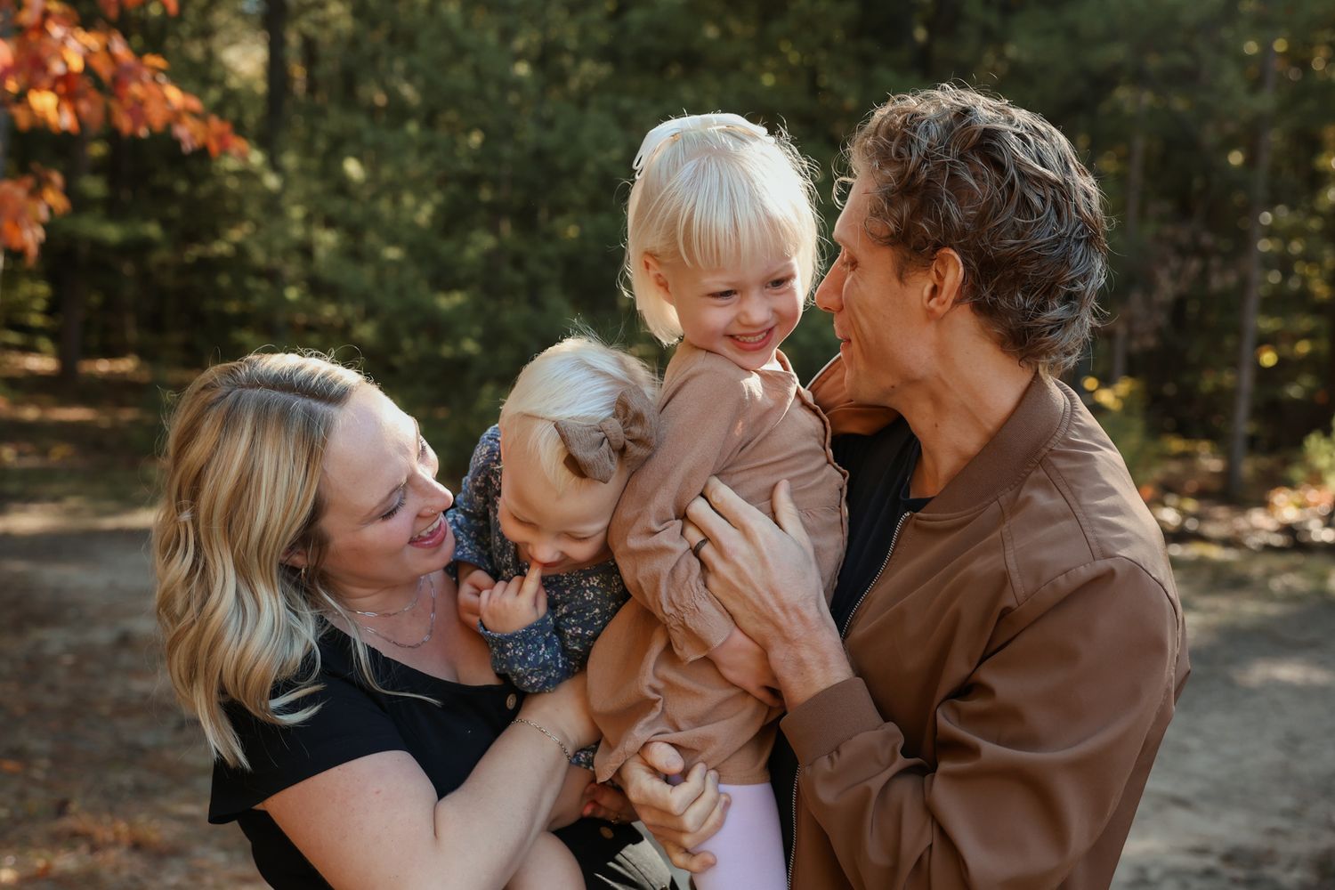 Joyful family with two young blonde children laughing together in an autumn forest setting.