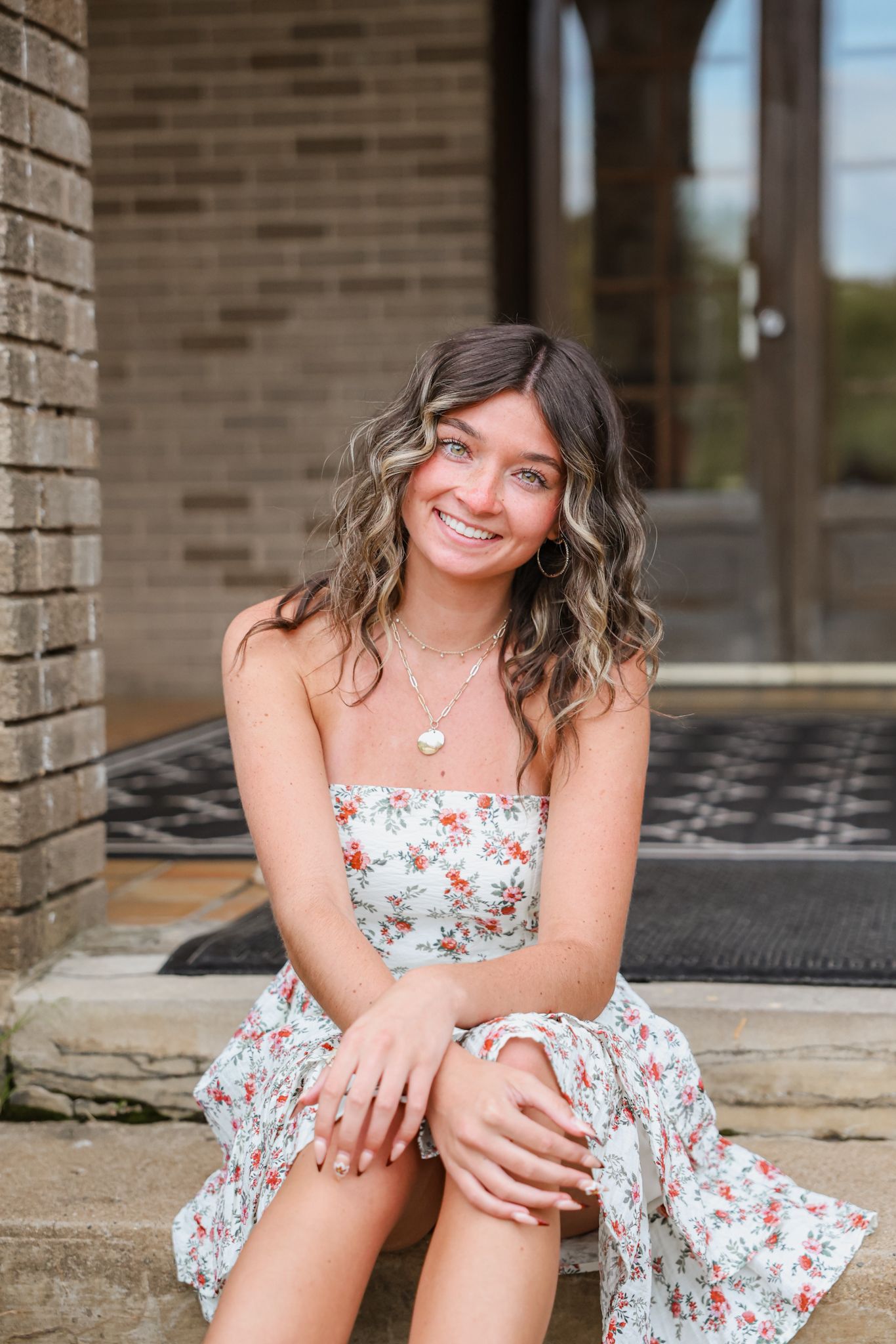 Smiling young woman in floral dress sitting on brick building steps.