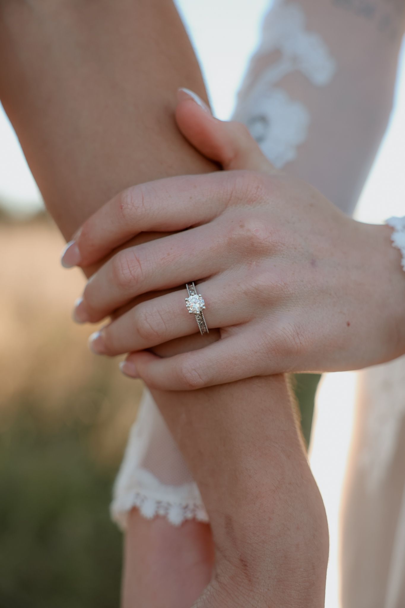 Close-up of a woman's hand with a diamond solitaire engagement ring resting on her partner's arm.