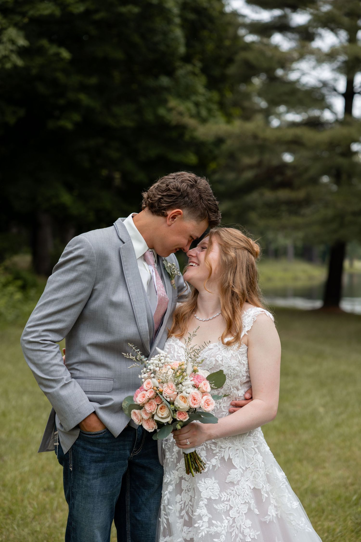 Bride and groom touching foreheads and smiling in a lush green outdoor wedding setting.