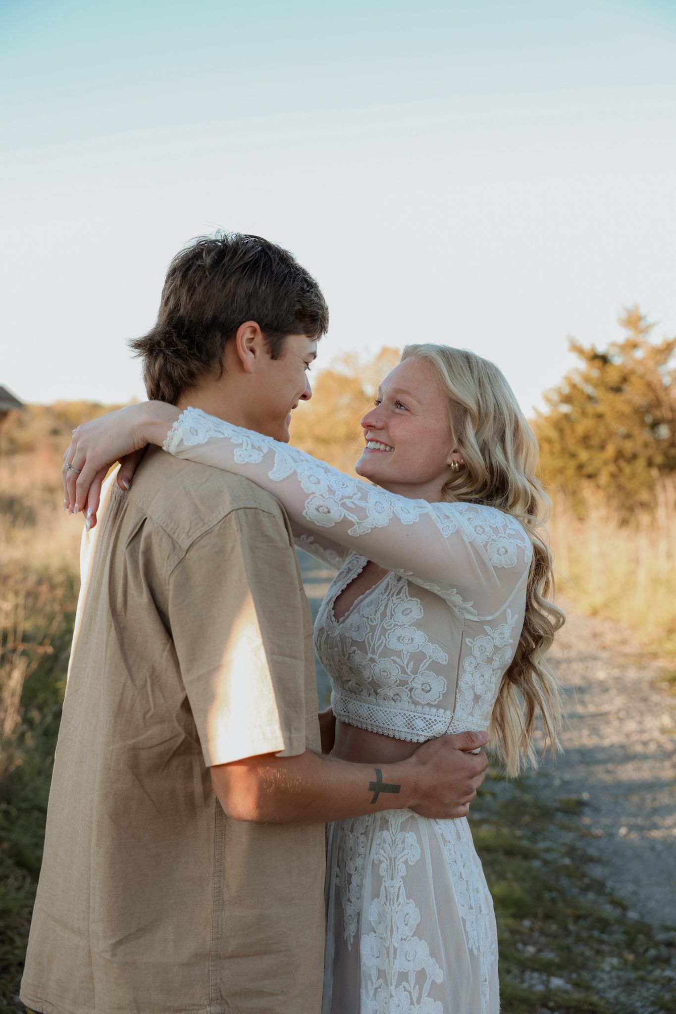 Joyful couple embracing and smiling at each other on a scenic rural path at sunset.