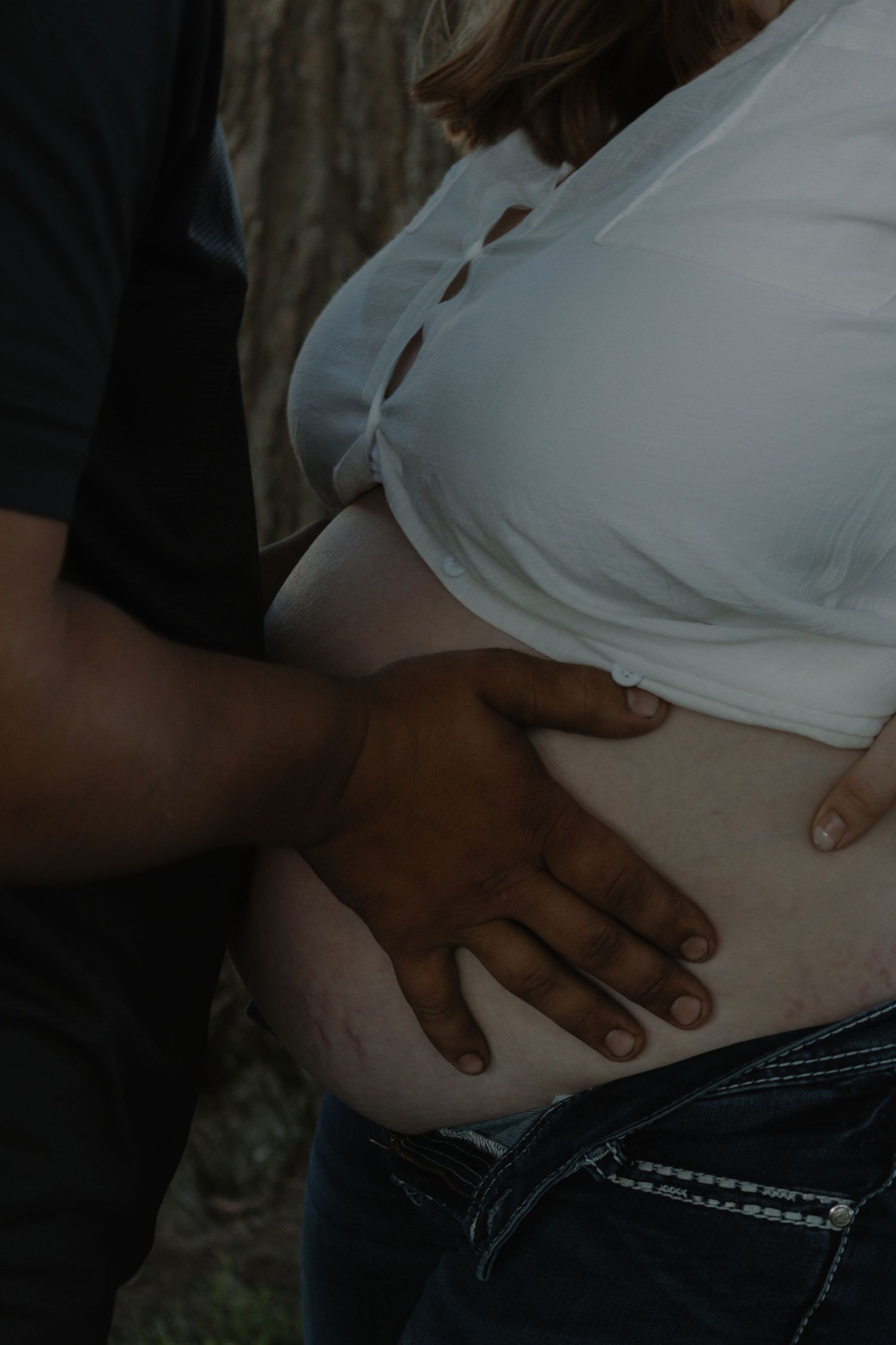 Intimate close-up of pregnant woman's bare baby bump with partner's hand gently resting on it.