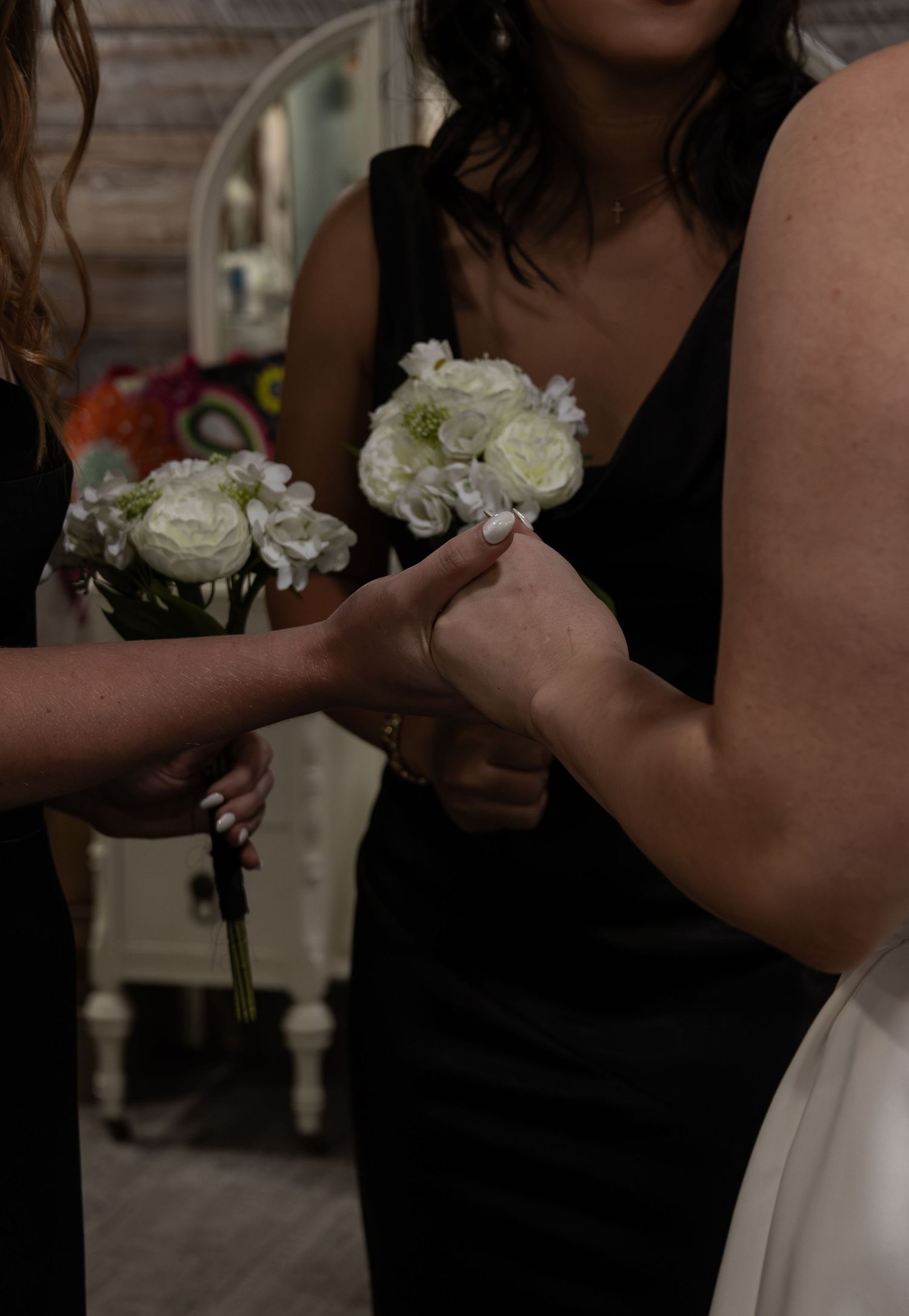 Bridesmaids in black dresses exchanging white rose bouquets at elegant wedding ceremony preparation.