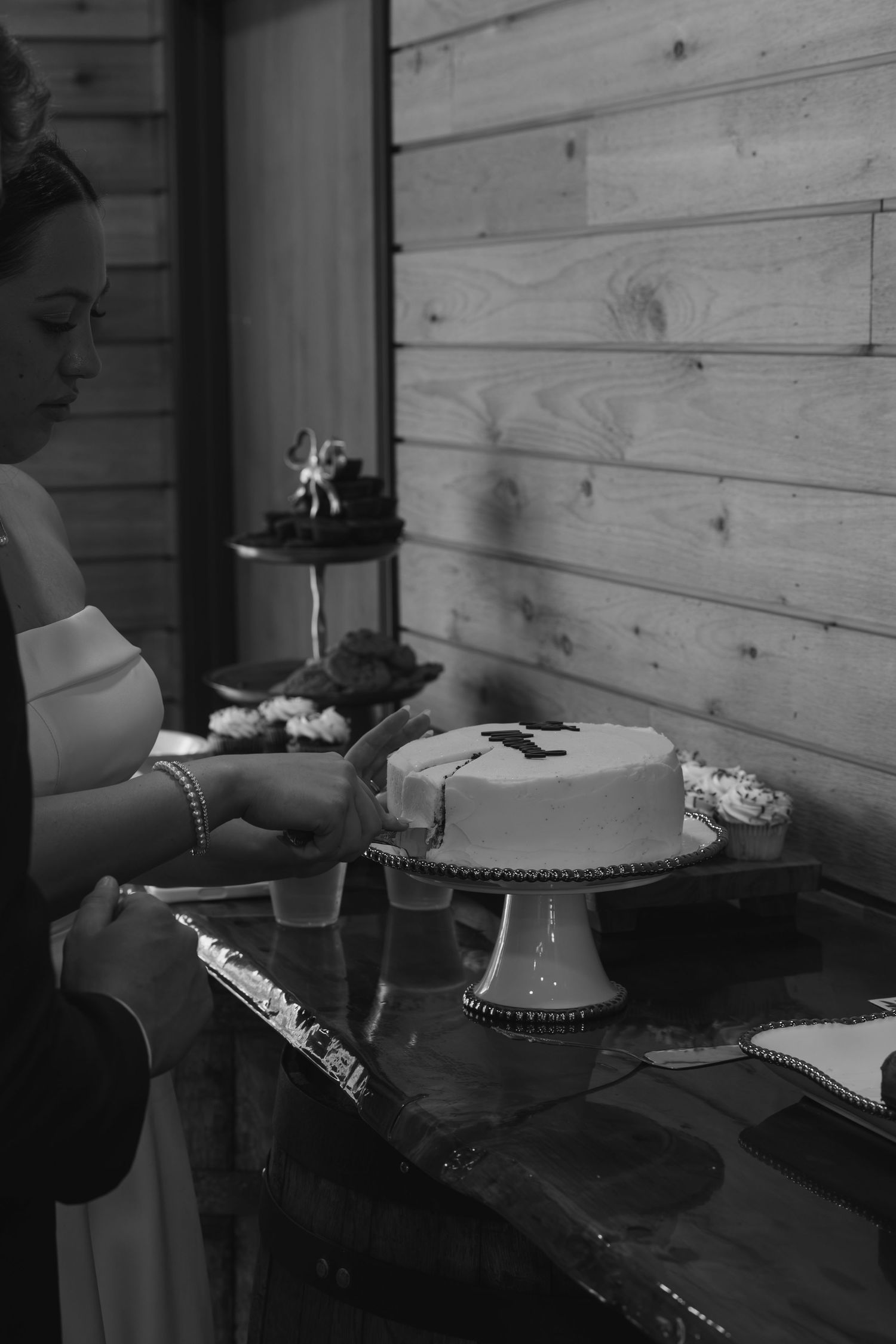 Black and white photo of a woman cutting a white cake on a pedestal stand at an elegant event.