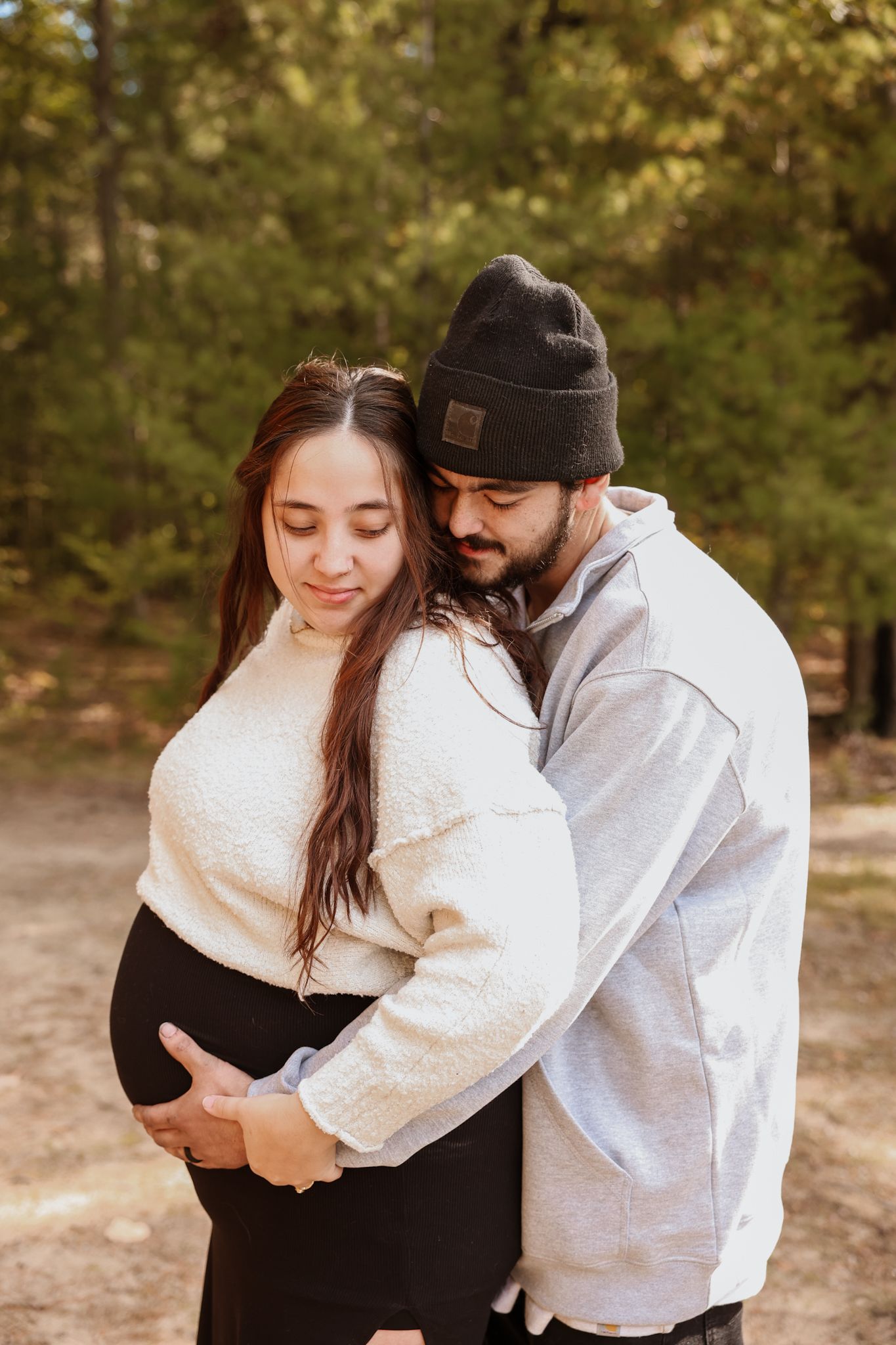 Tender maternity photo of couple embracing outdoors in autumn forest, man holding pregnant woman's belly.