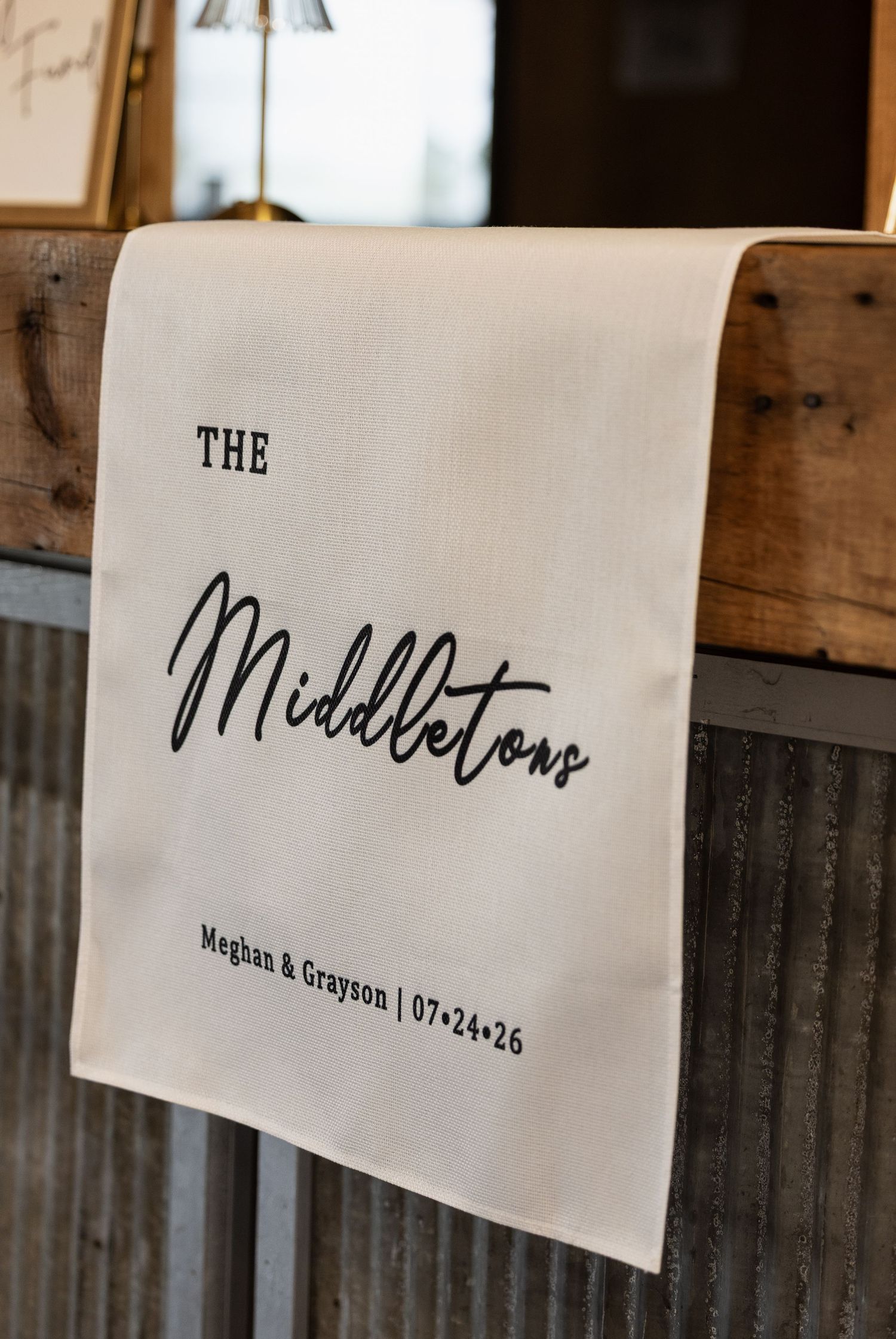 Personalized wedding tea towel for The Middletons, Meghan & Grayson, dated 07-24-26, draped over rustic wood.