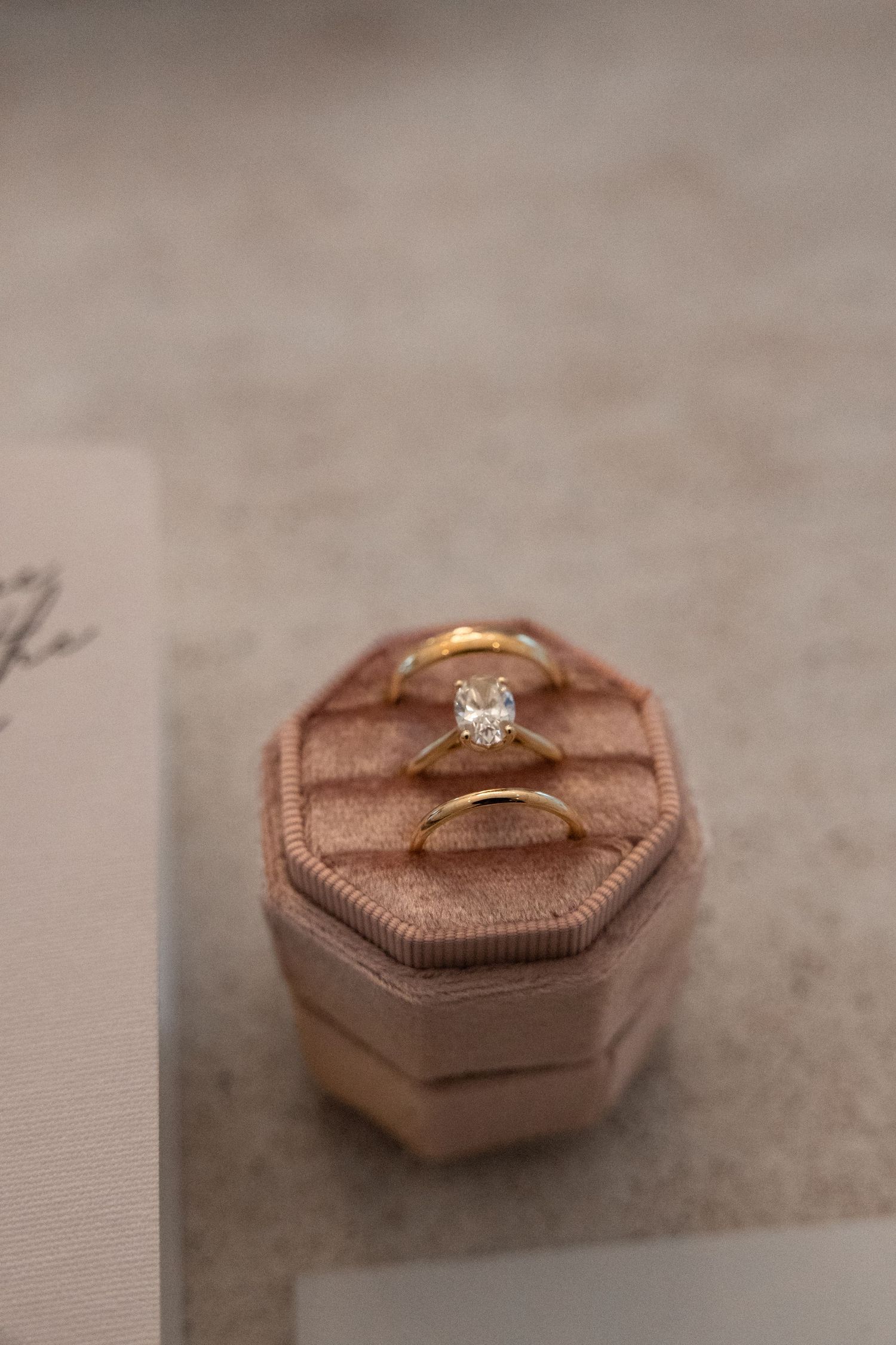Three gold wedding rings displayed in a pink velvet octagonal ring box on neutral background.