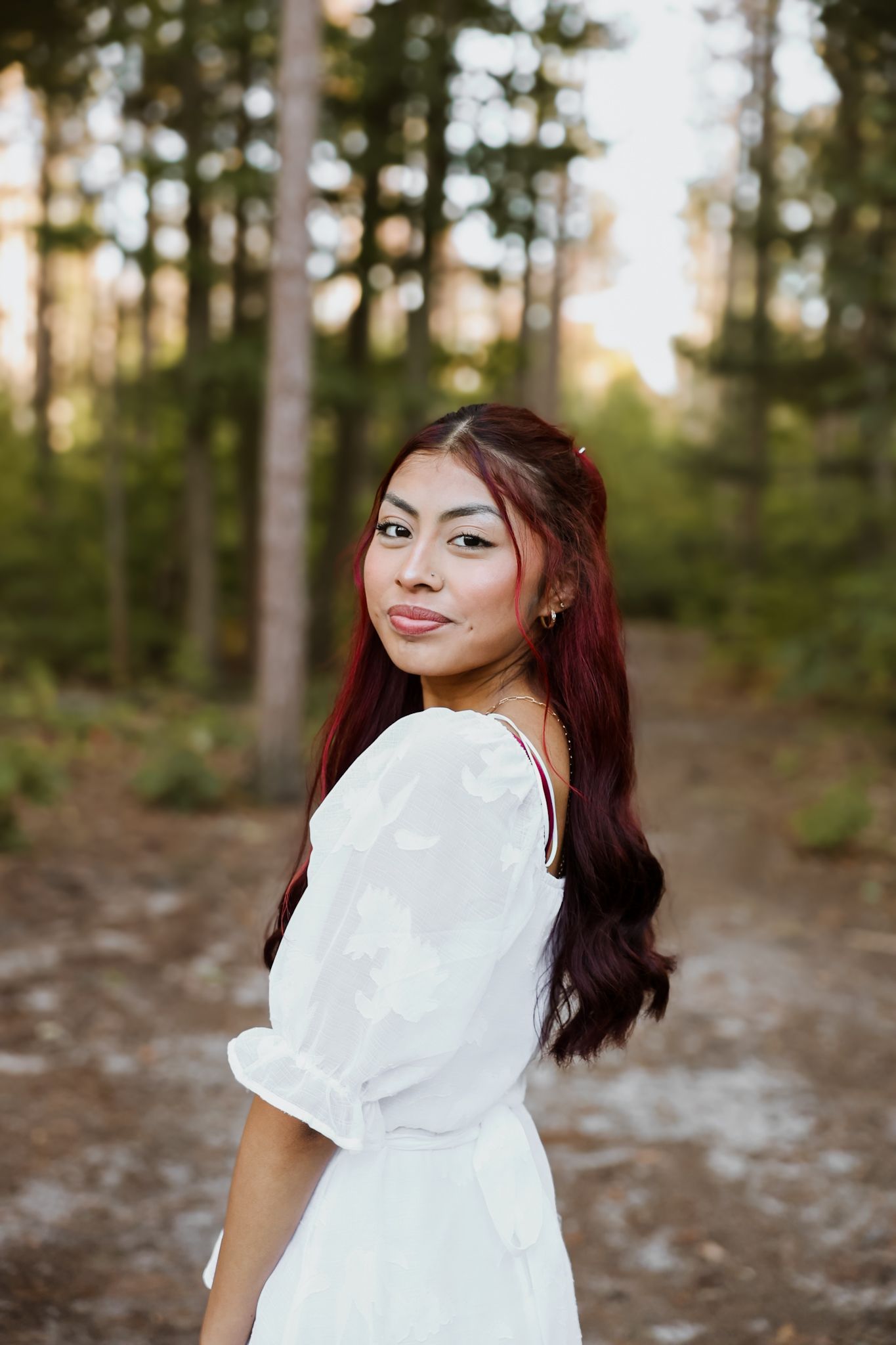 Young woman in white dress smiling over shoulder on forest path.
