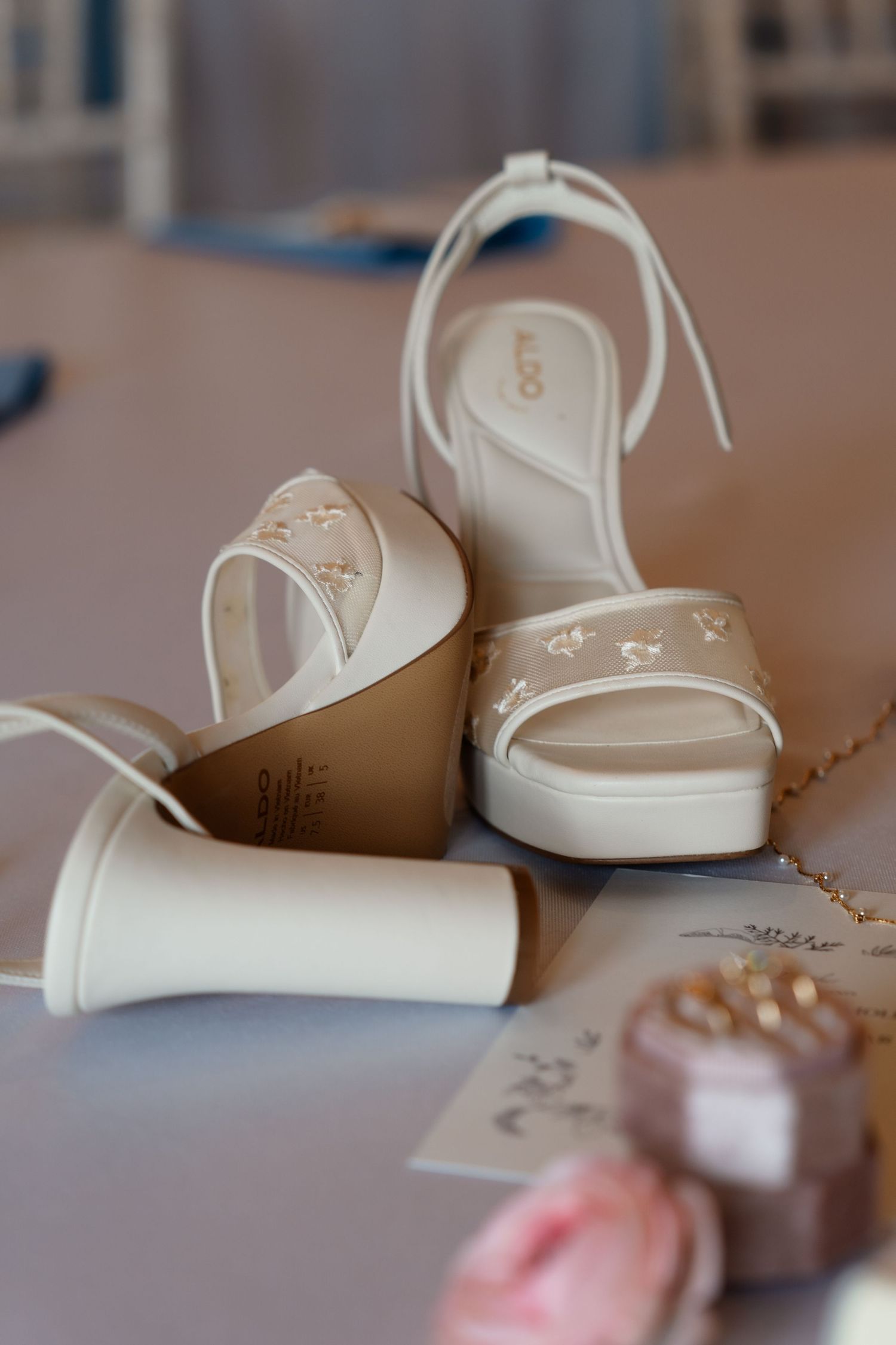 White ALDO platform bridal heels with delicate floral details displayed beside wedding accessories.
